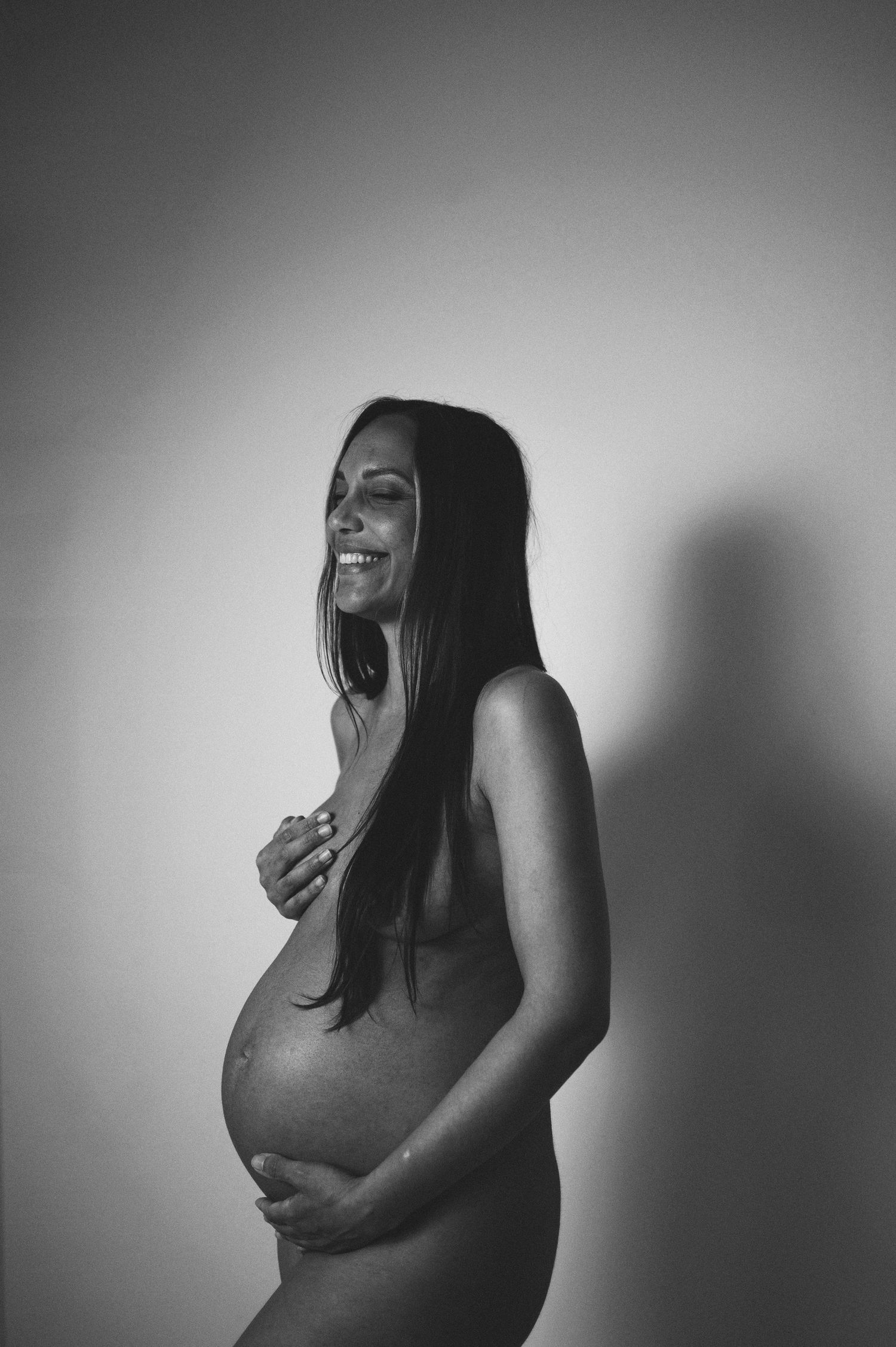 Smiling pregnant woman posing in black and white maternity portrait.