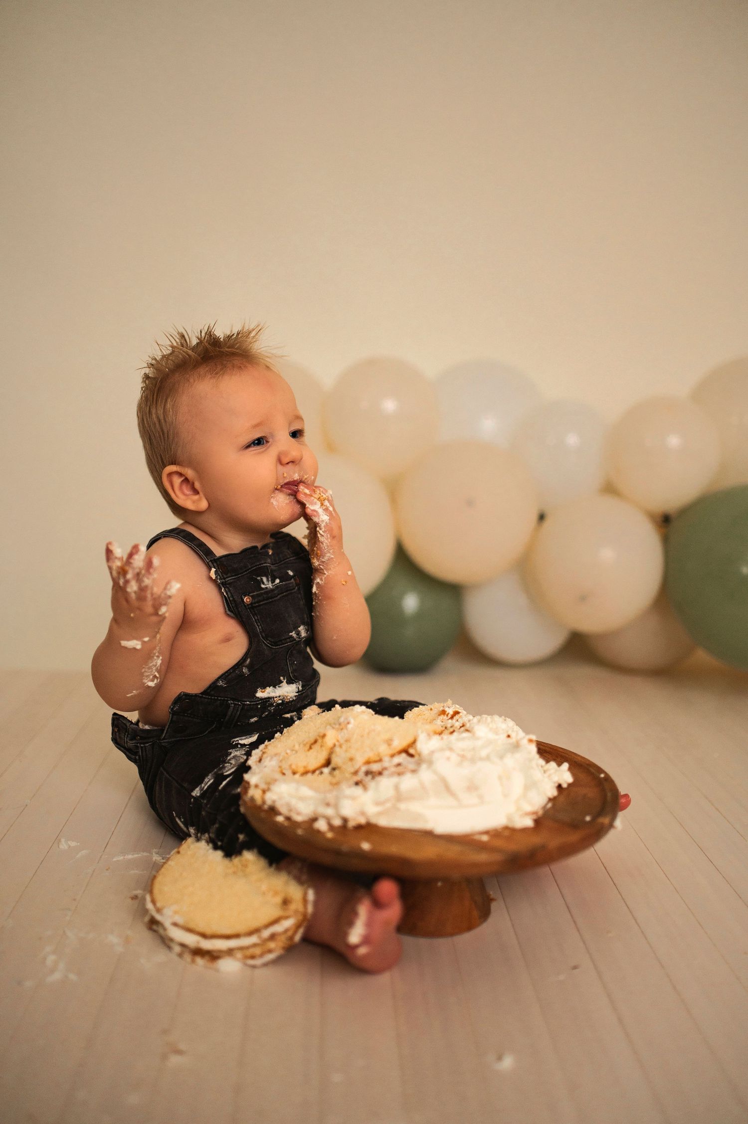 A messy cake smash photoshoot with white and sage green balloon decorations.