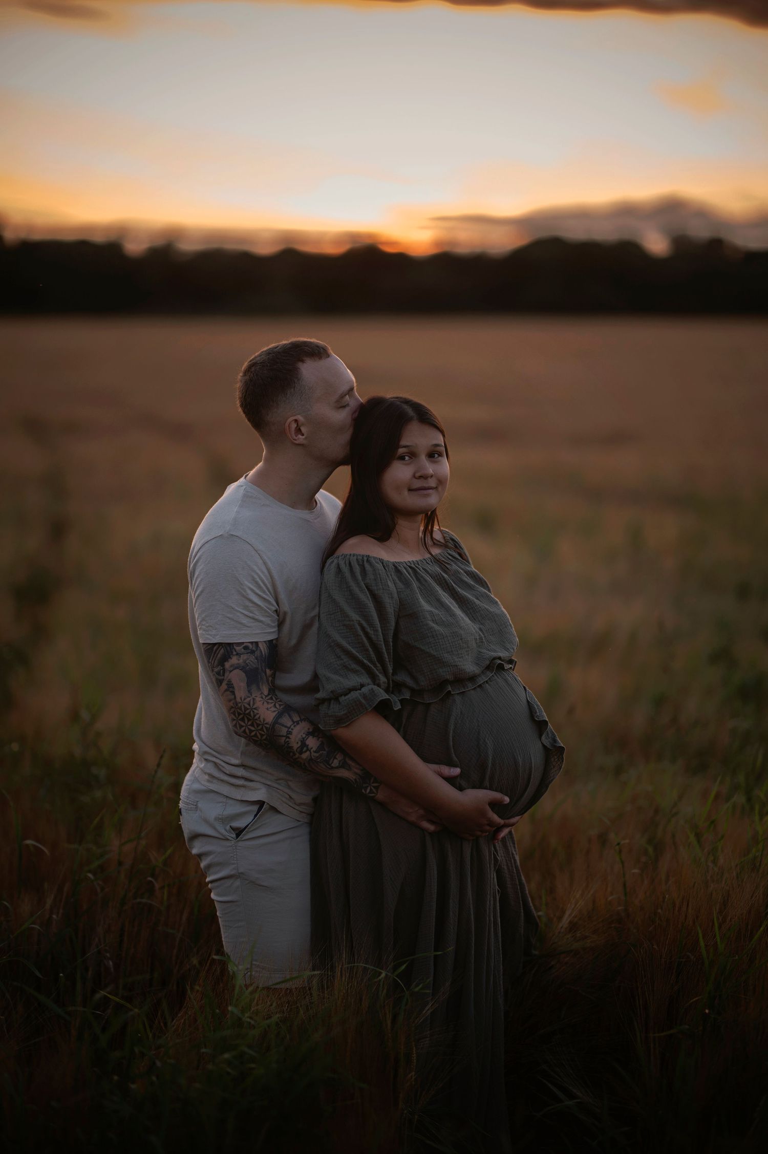 A romantic sunset maternity photo of a couple standing together in a rural field.