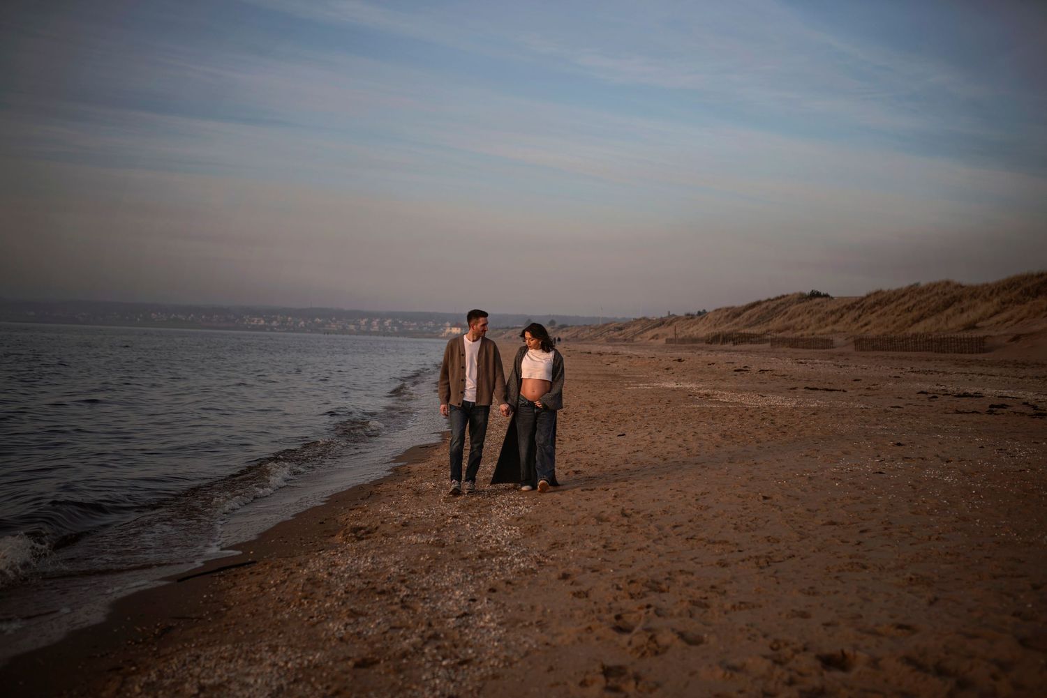 Two people strolling along the shoreline at dusk.
