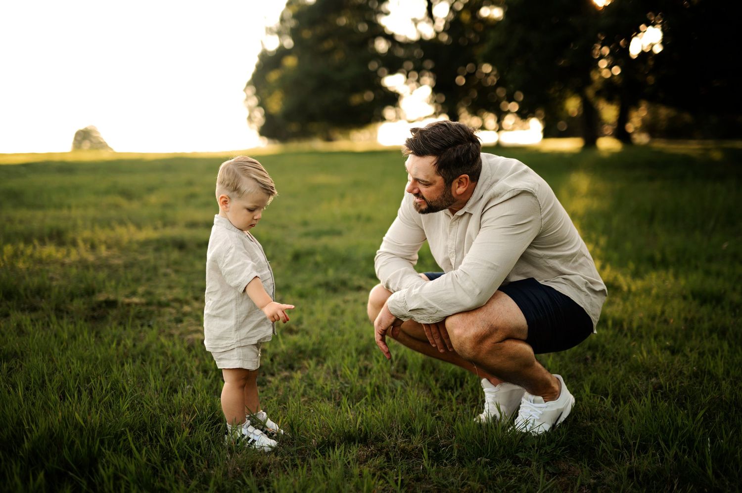 Parent and toddler interact playfully on grassy hill at sunset.