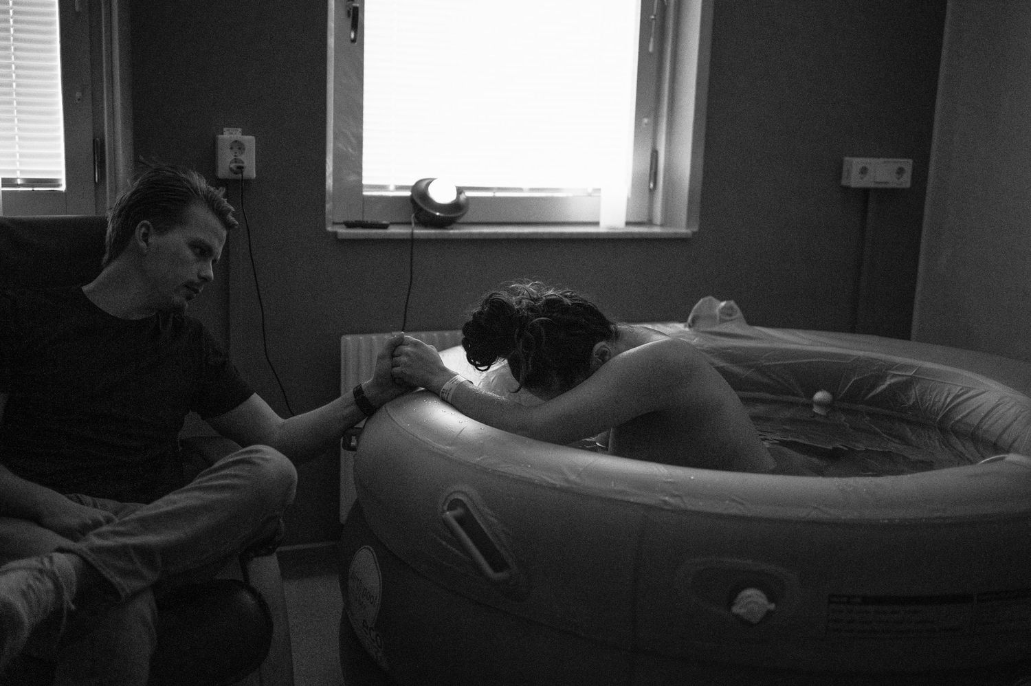 A person provides support during labor in a dimly lit room with an inflatable birthing pool.