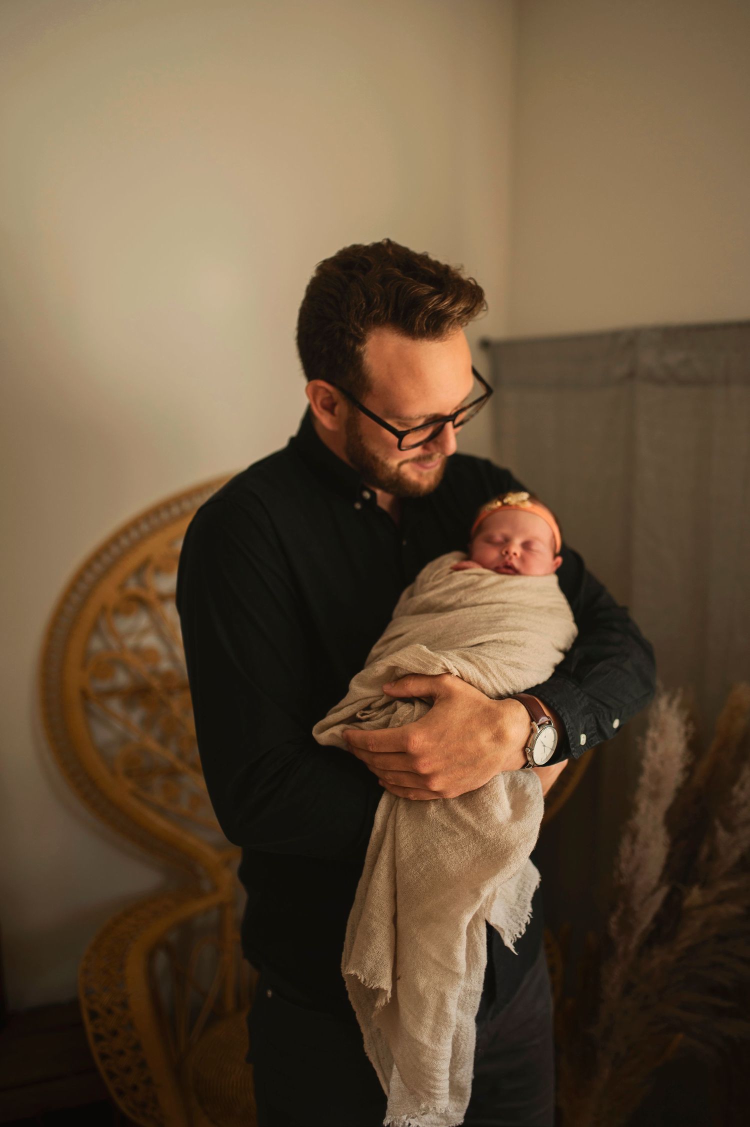 A tender moment captured as a parent in black clothing cradles a sleeping newborn baby wrapped in white.