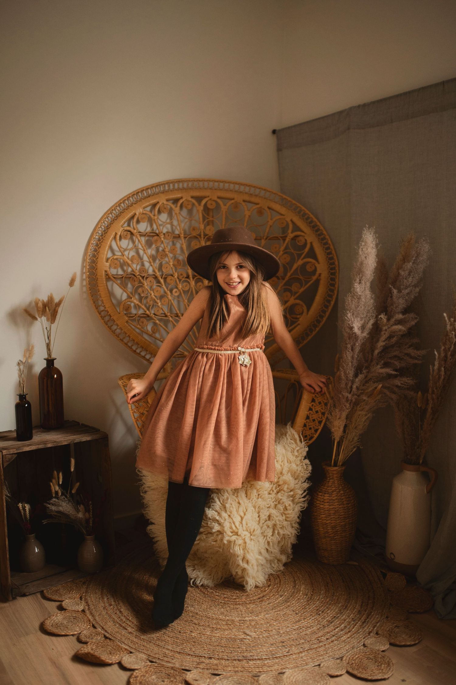 Dancing figure in a brown dress and hat poses against a bohemian backdrop with dried flowers.