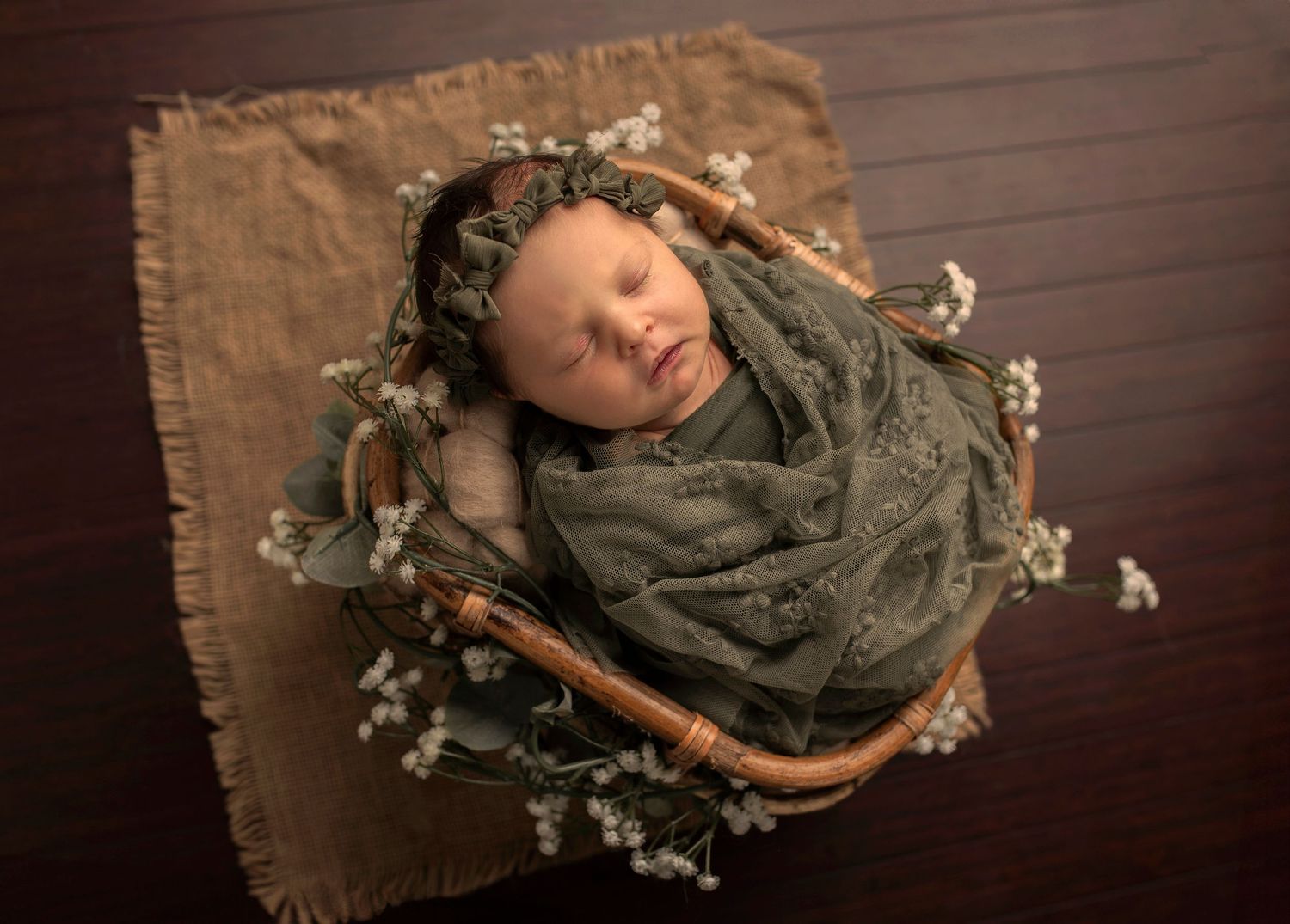 Sovande nyfödd bebis i korg under en nyföddfotografering i Hässleholm i mjuka gröna och naturliga toner.