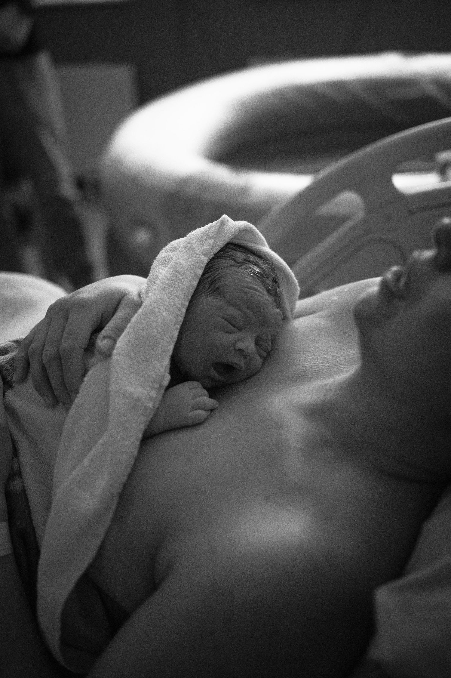 A newborn baby rests bundled in a white towel after birth in a black and white photograph.