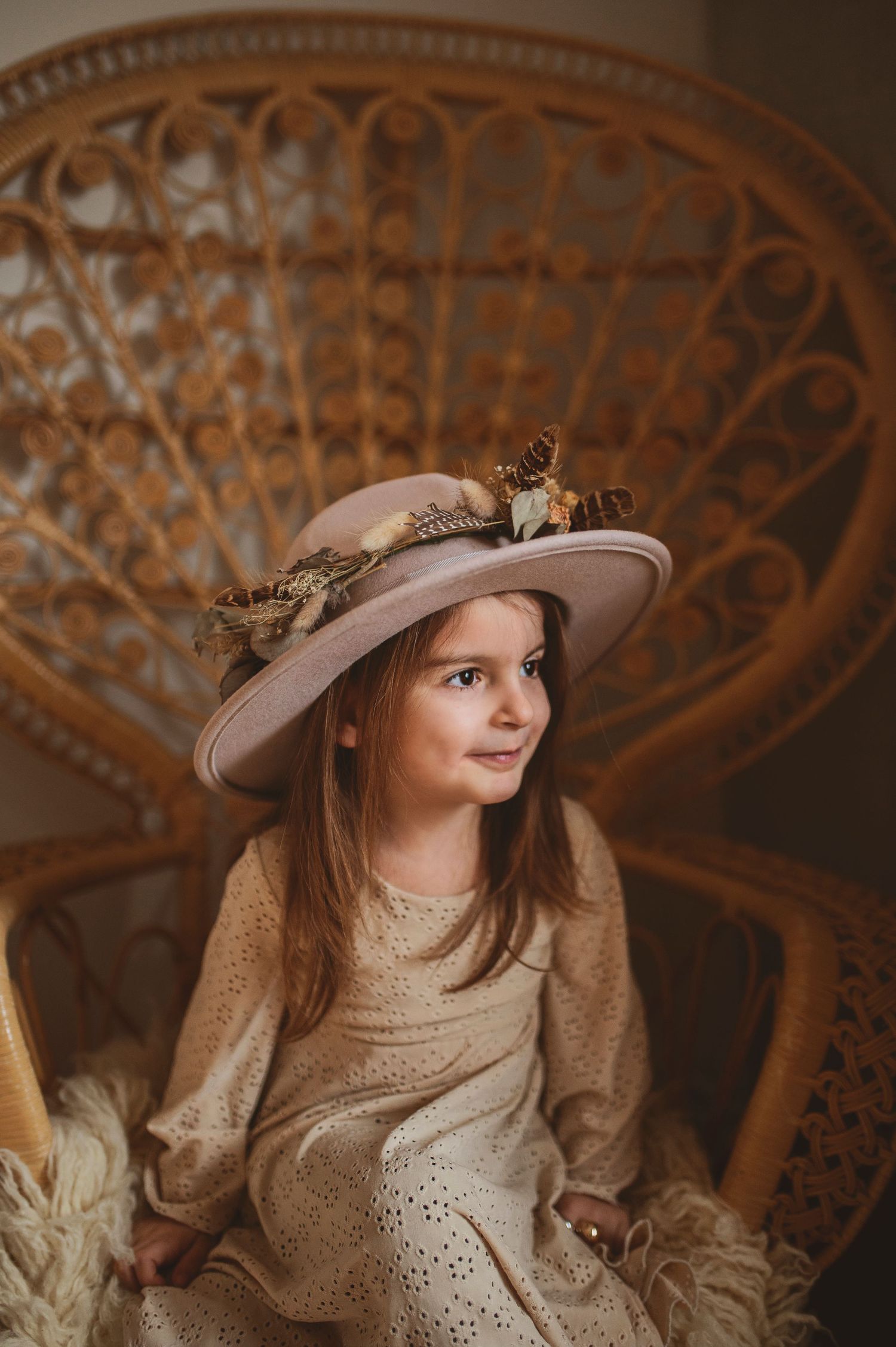 A decorative hat adorned with flowers complements a lace dress against an intricate woven backdrop.
