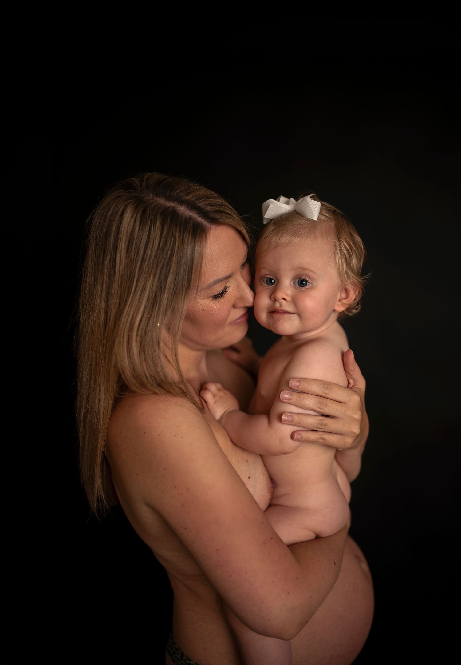 Artistic maternity portrait with mother and baby against dark background.