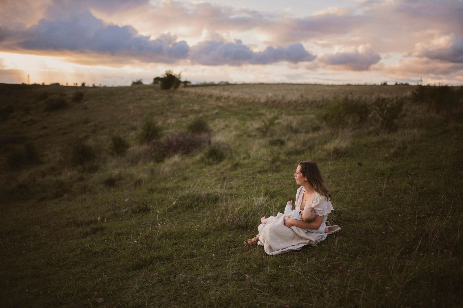Amningsfotografering i Skåne på Hilleshögs Dalar med mamma i vit klänning i dramatiskt landskap.