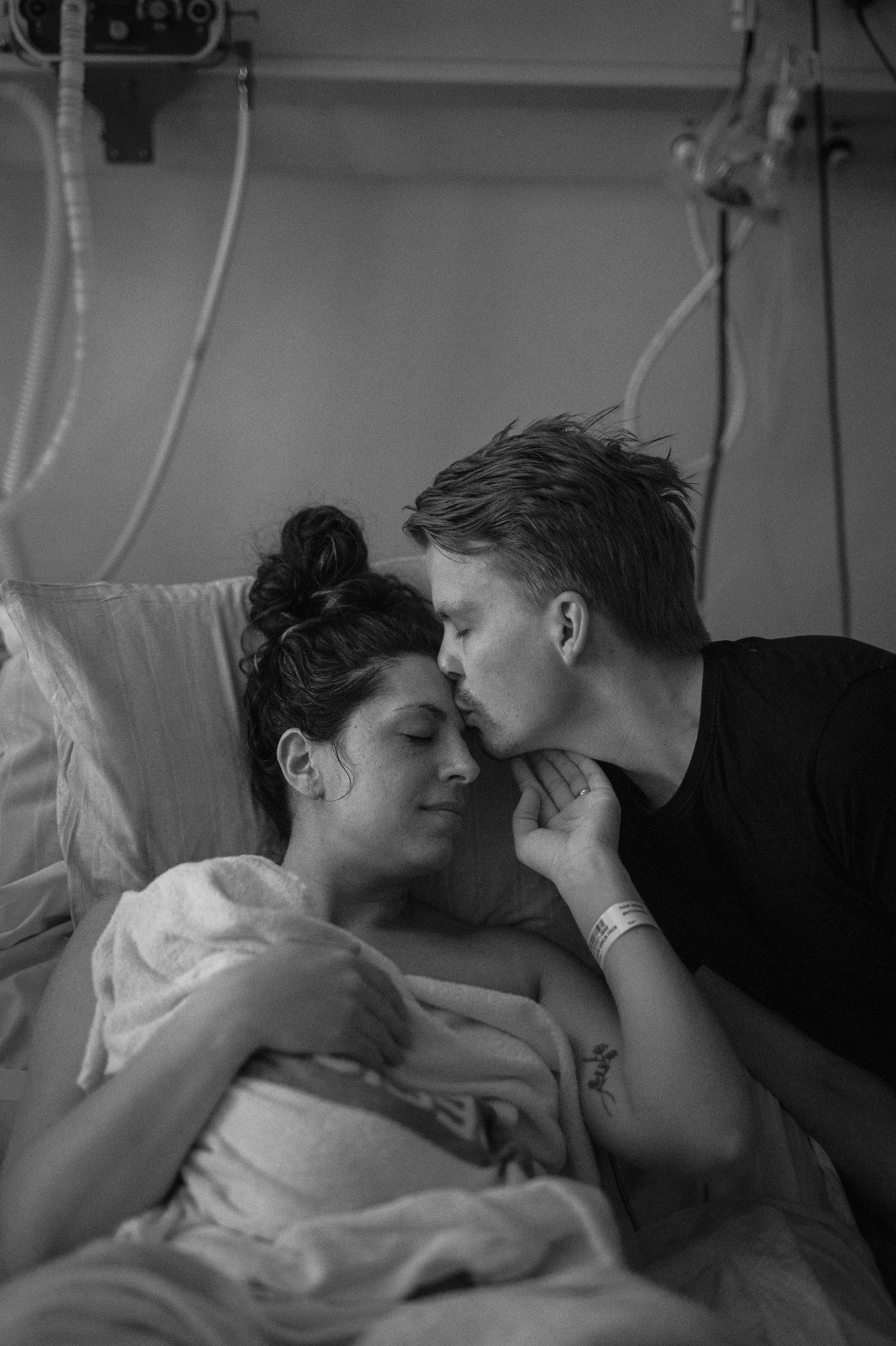 Svartvit förlossningsfotografering i Skåne med partner som kysser mamma i förlossningsrummet.
