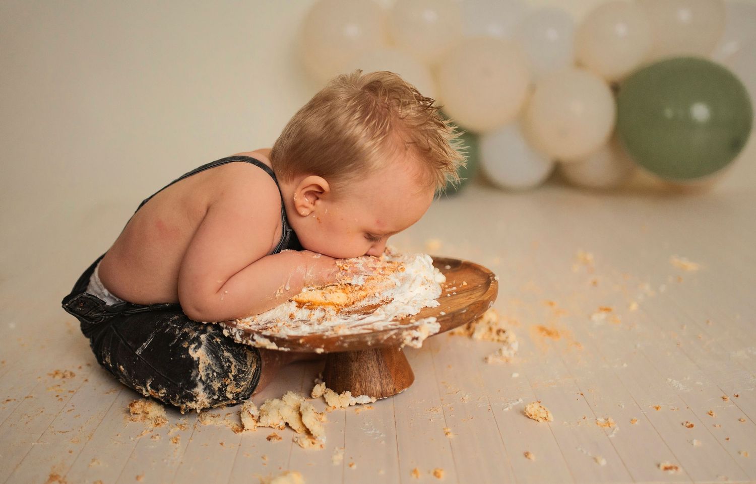 A creative cake smash photo featuring messy frosting and a rustic wooden cake stand.