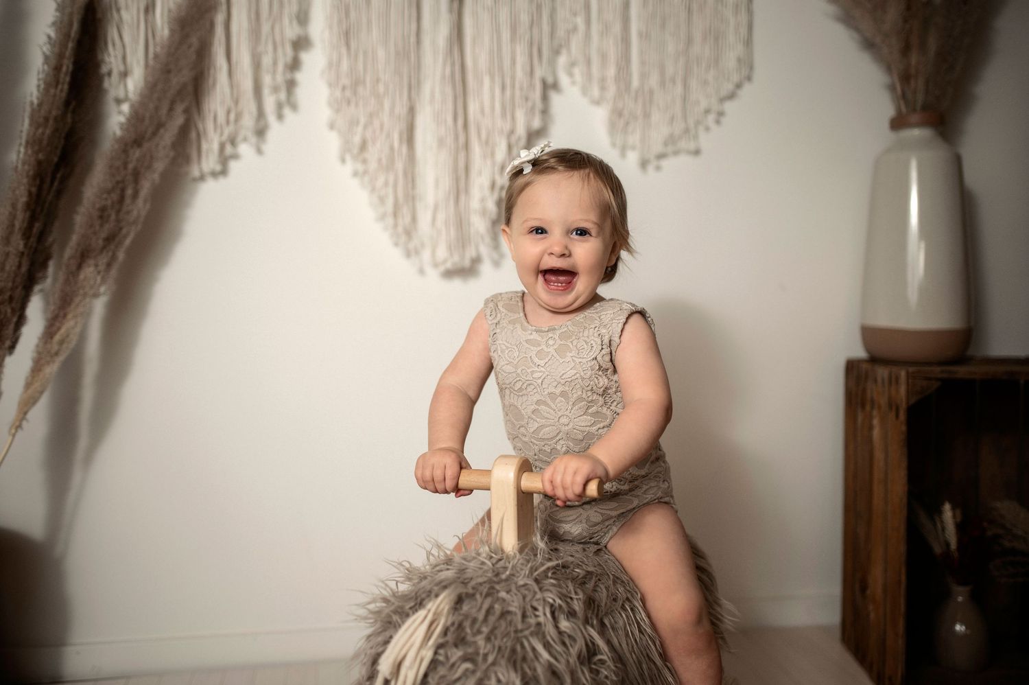 Leende bebis på gunghäst under en barnfotografering i studio i Hässleholm med bohemisk inredning.