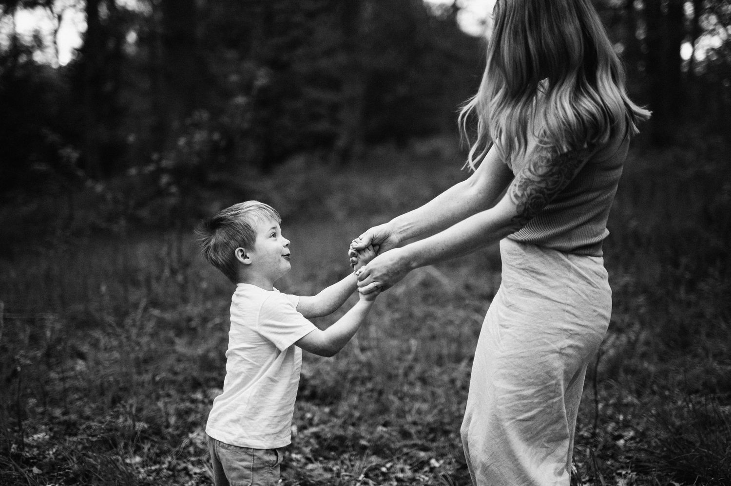 Familjefotografering i Skåne med pojke som håller sin mammas hand i skogsmiljö i svartvitt ljus.