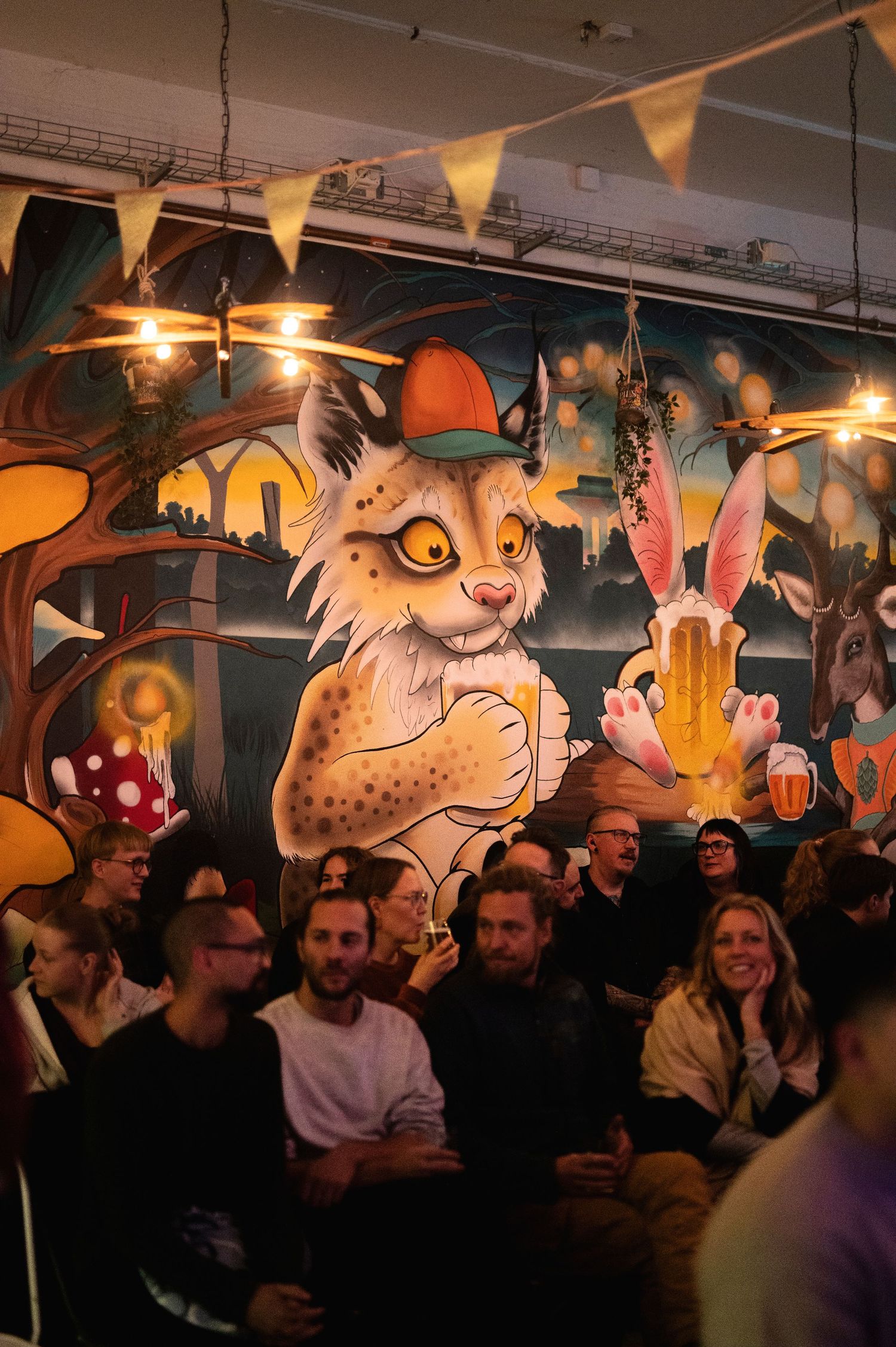 Eventfotografering i Skåne med barinteriör och gäster framför färgstark väggmålning med skogsdjur.