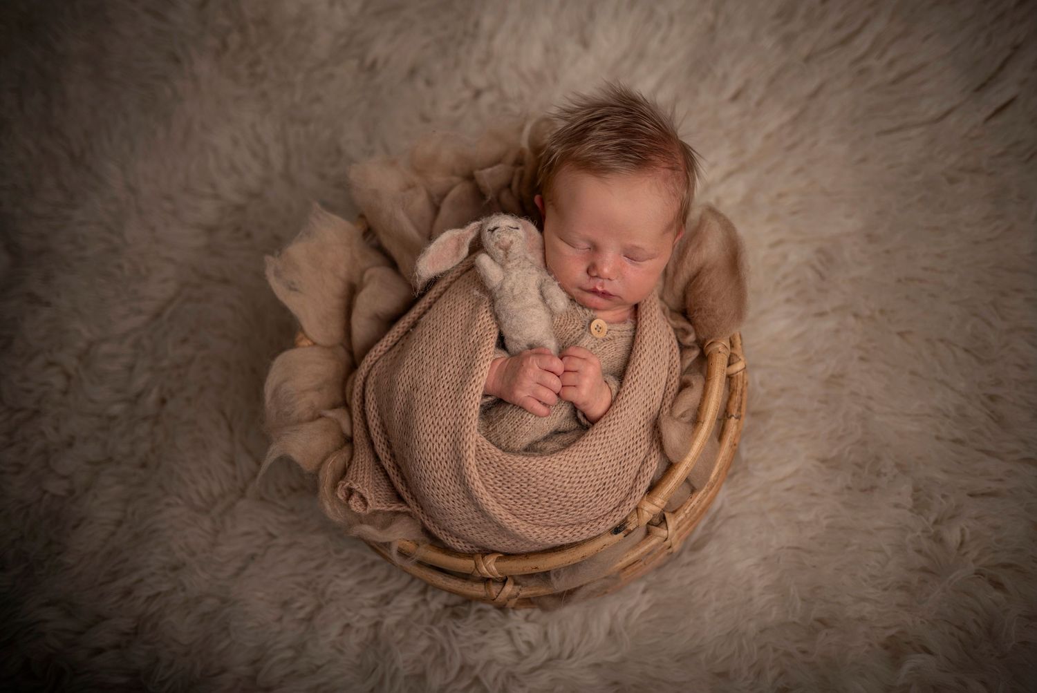 Sovande nyfödd bebis i korg under en nyföddfotografering i Hässleholm i mjuka beiga toner.
