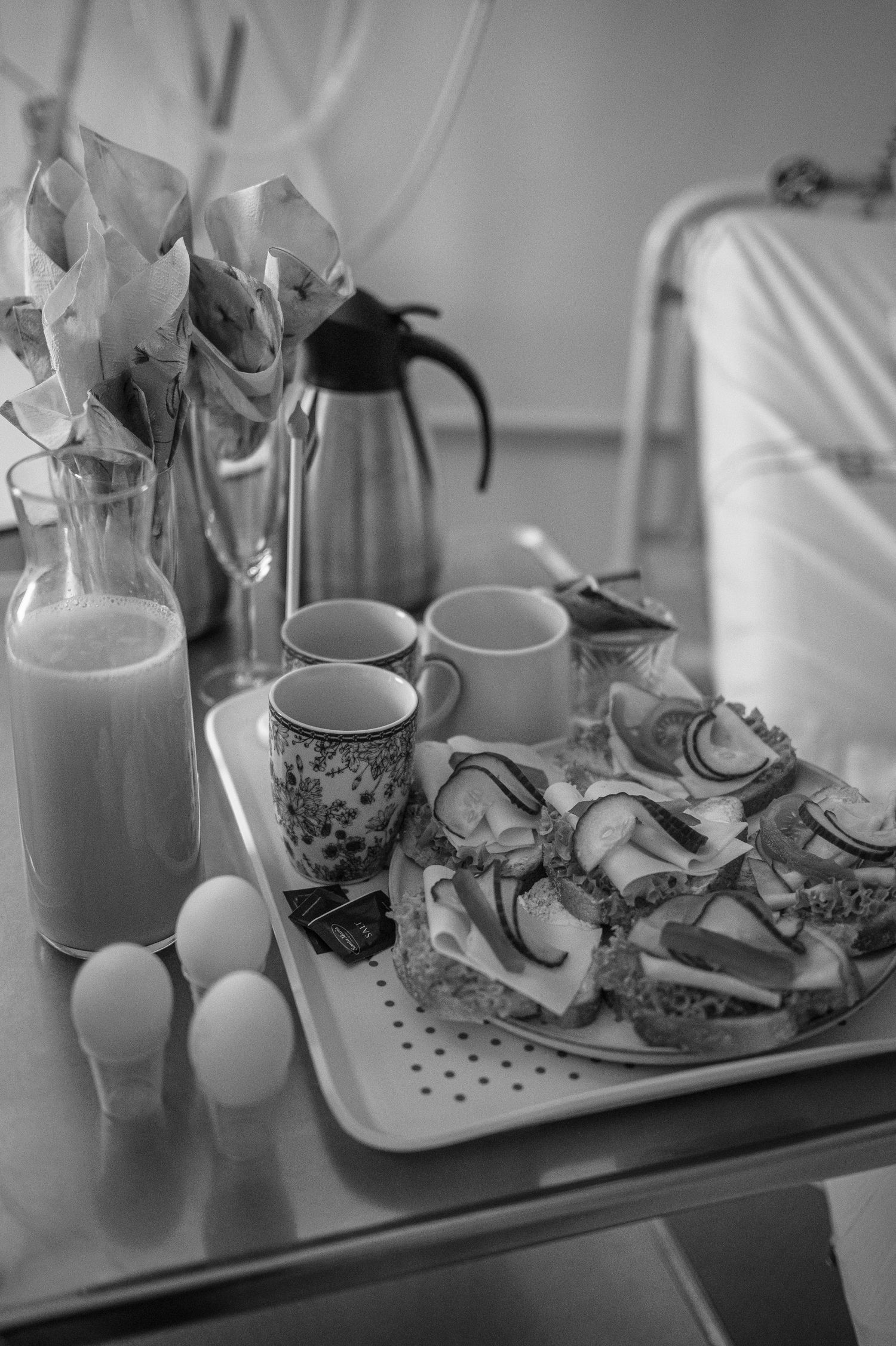 Black and white breakfast scene with sandwiches, eggs, coffee cups and a bottle of milk on a table.