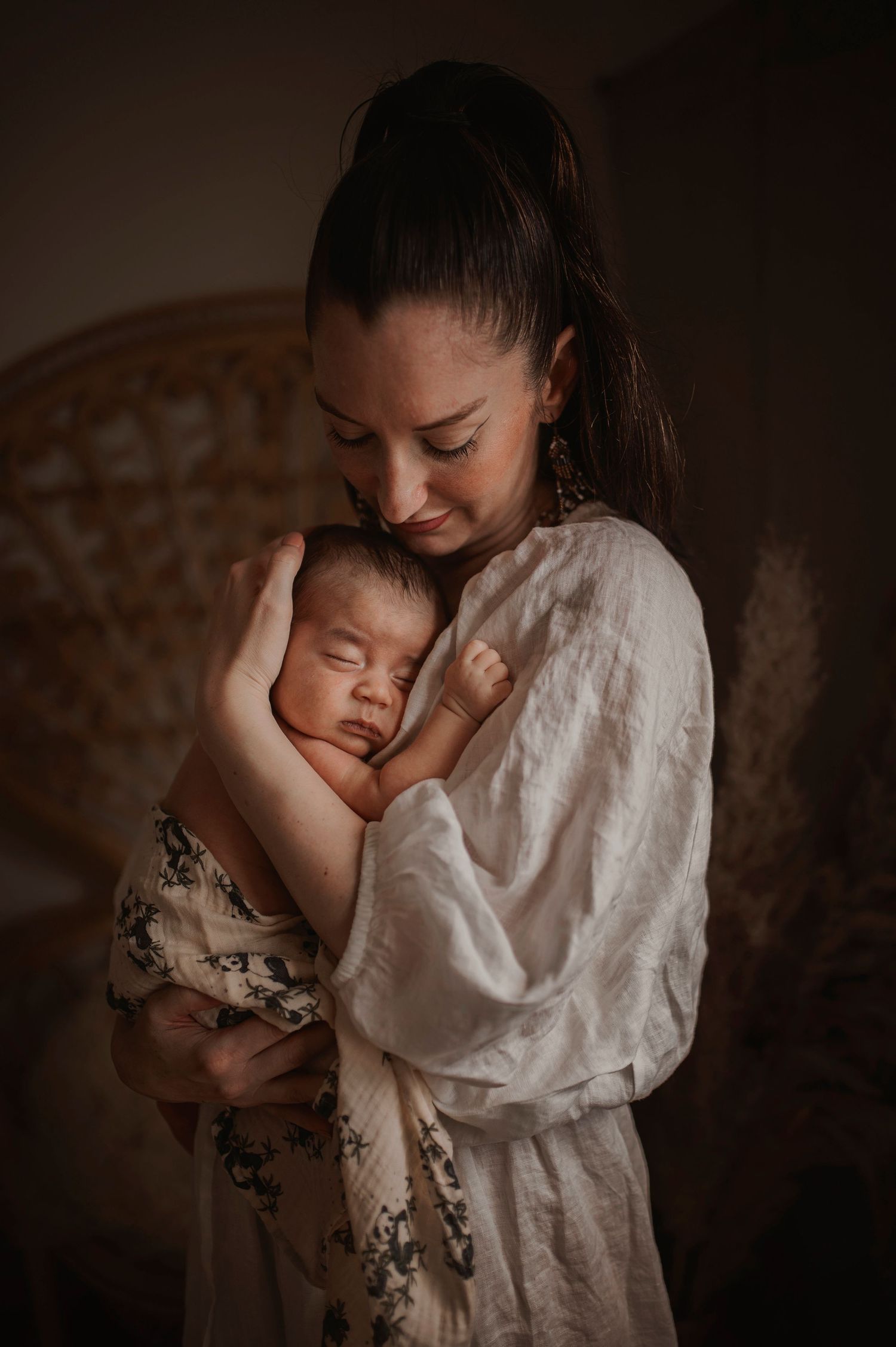 Gentle portrait of caregiver in white dress holding sleeping infant in warm ambient light.