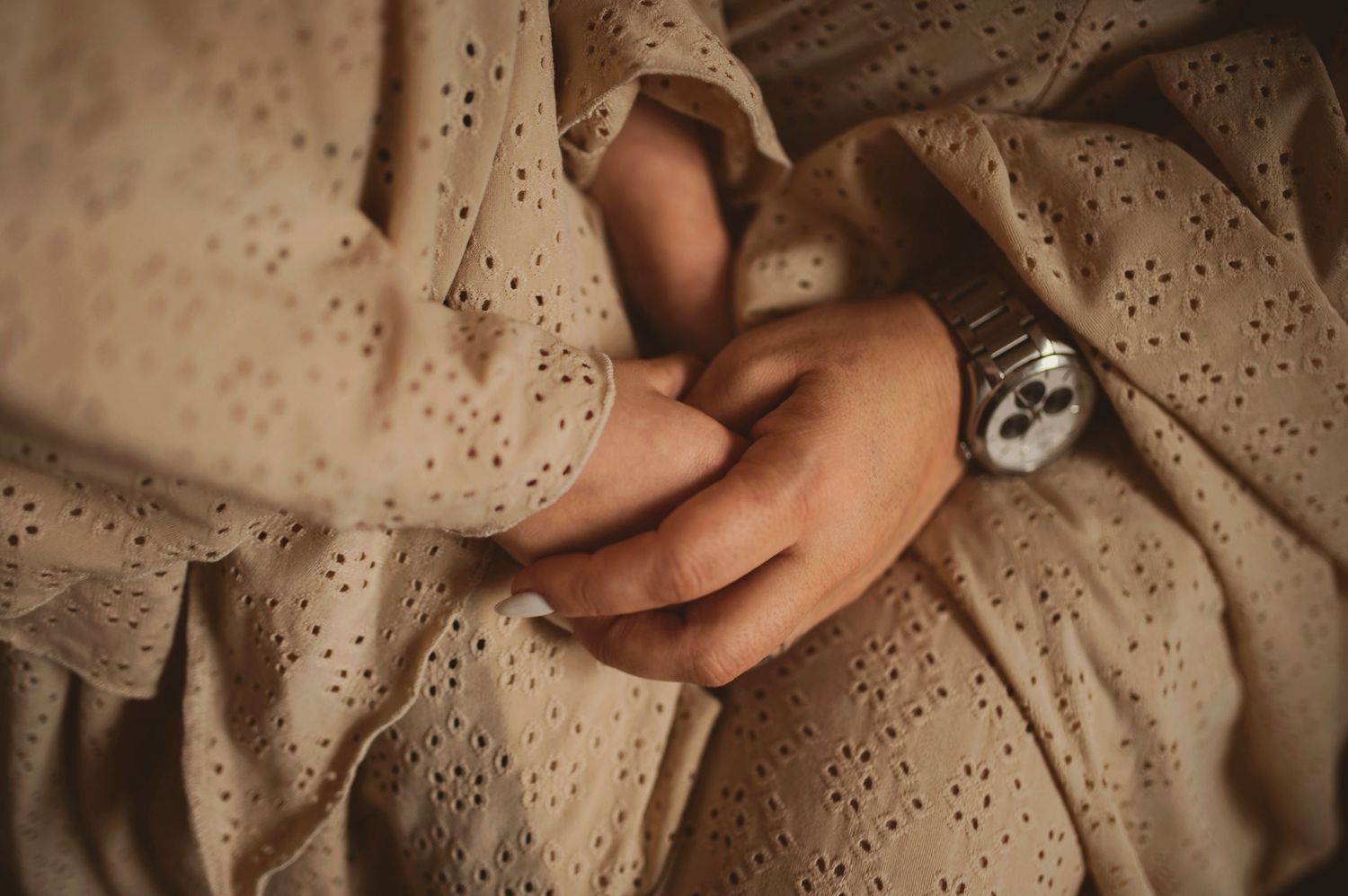 Close-up detail of hands against delicate eyelet lace fabric in soft beige tones.