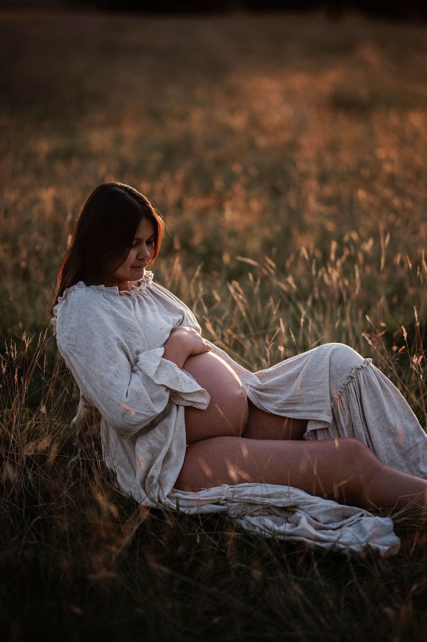 Expecting mother in white dress resting peacefully in golden field at sunset.