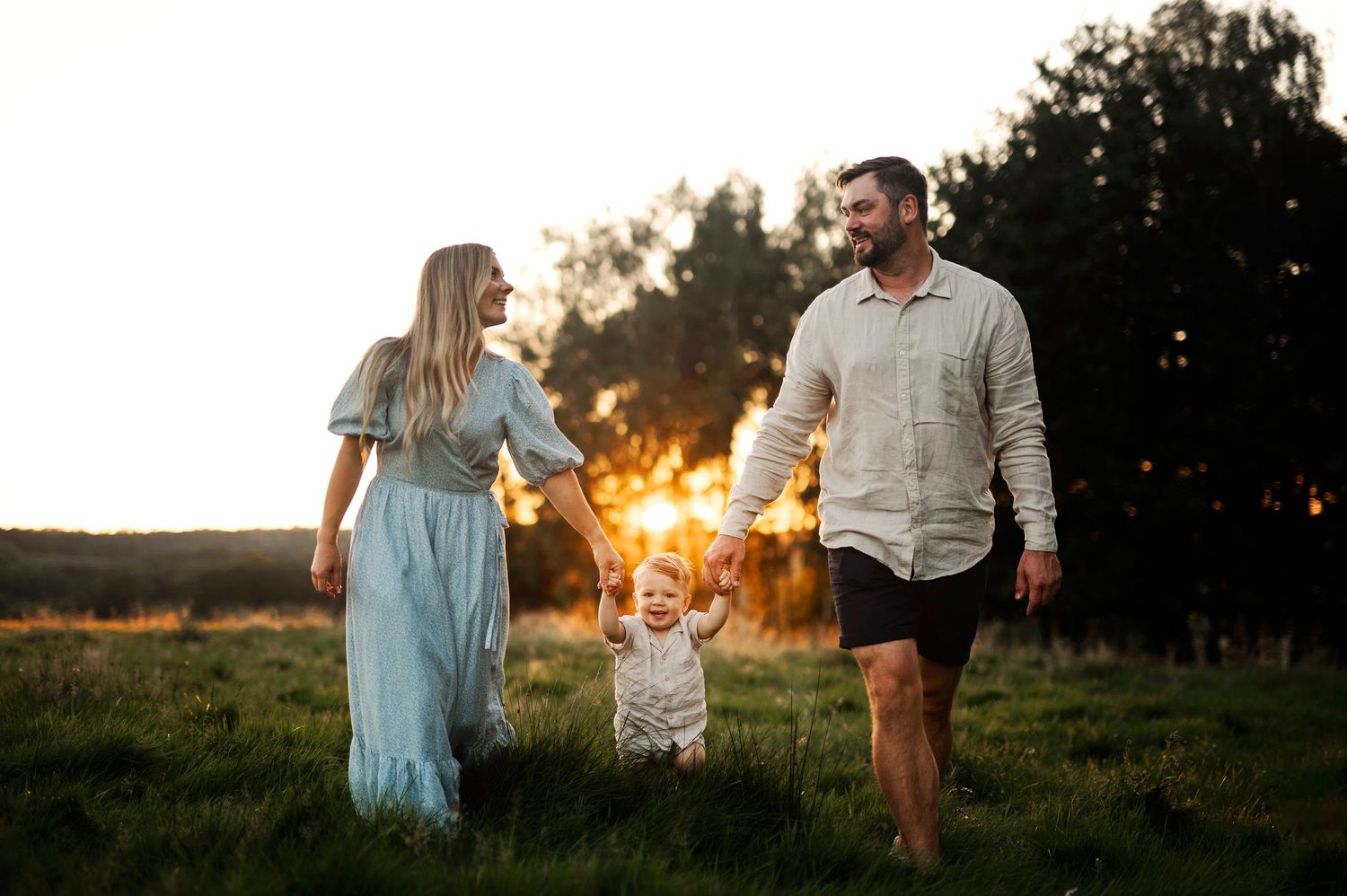 Familjefotografering i Skåne med familj som går i grön äng i solnedgång i gyllene motljus.
