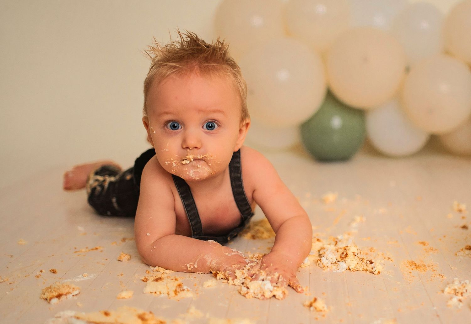 A playful cake smash portrait session with white and sage green balloon decorations.