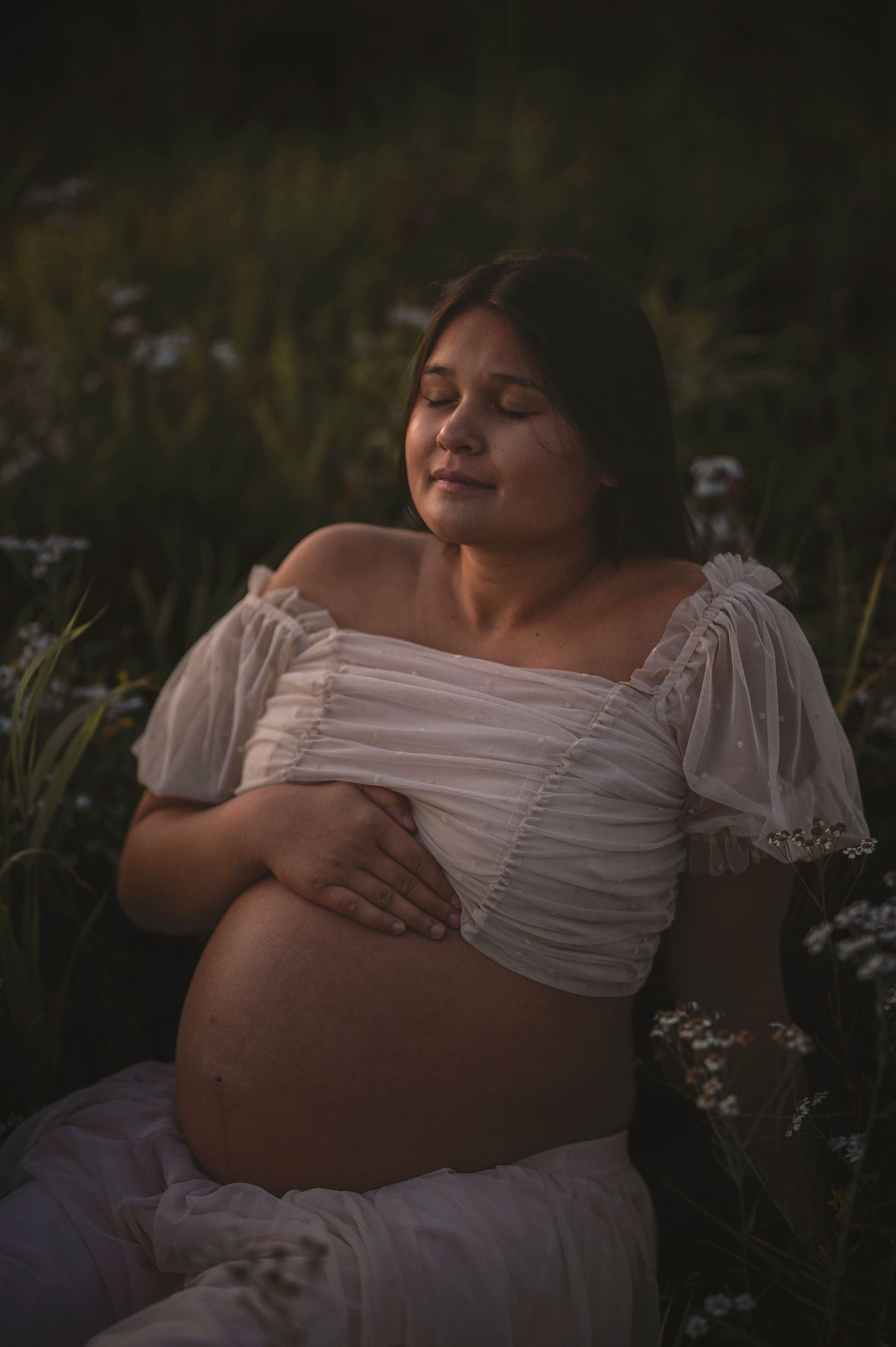 An intimate maternity portrait surrounded by delicate wildflowers at sunset.