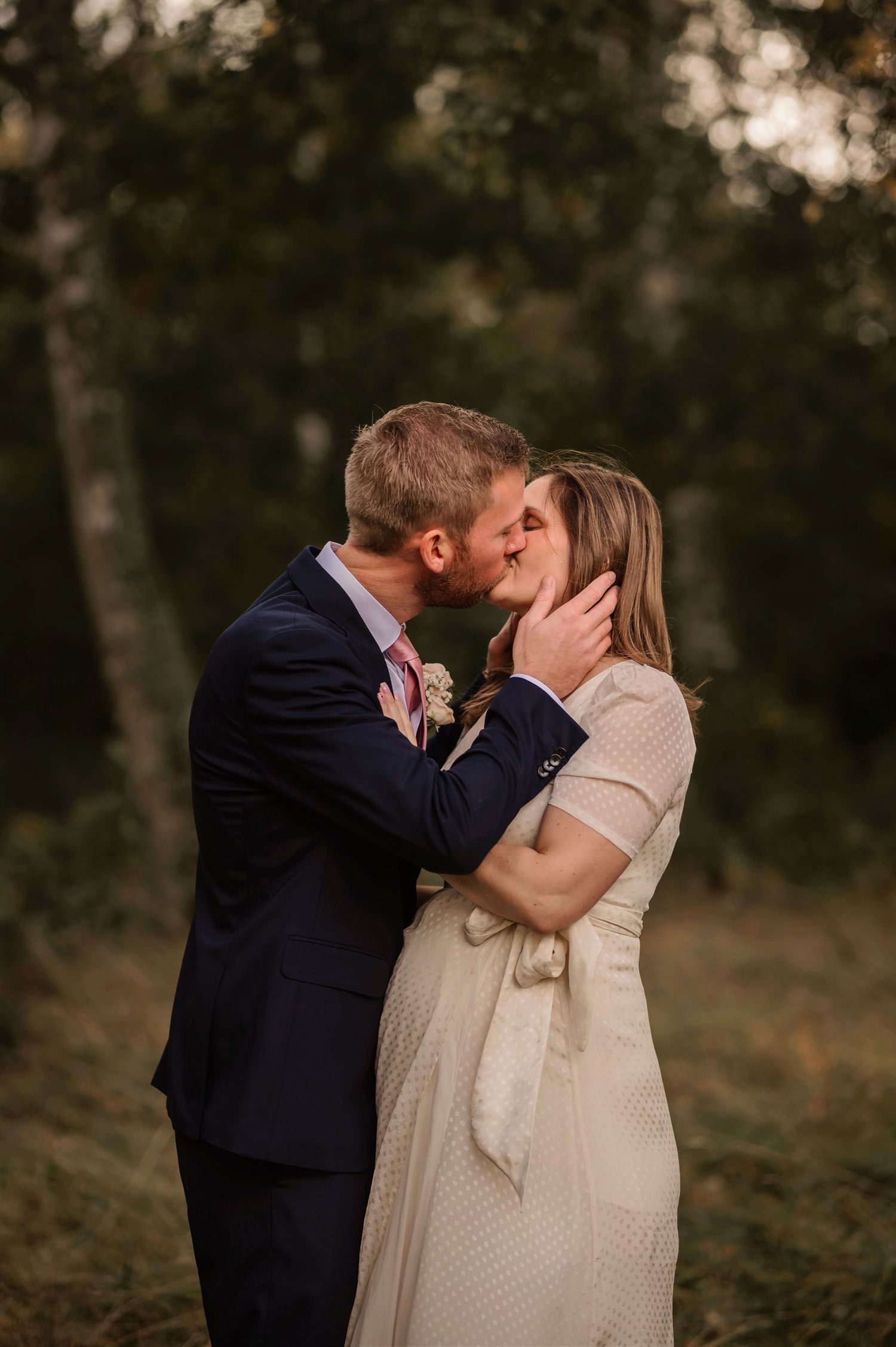 Bröllopsfotografering i Skåne med brudpar som kysser varandra i skogsmiljö i mjukt kvällsljus.