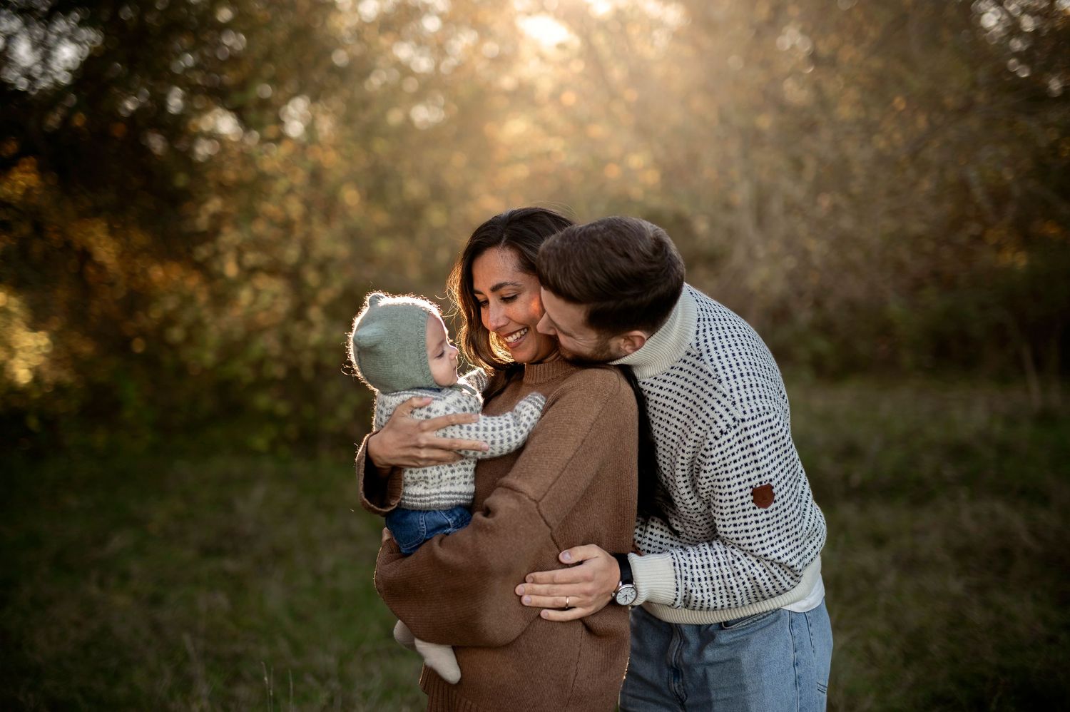 Familjefotografering i Skåne med föräldrar som myser med sitt skrattande barn i gyllene kvällsljus.