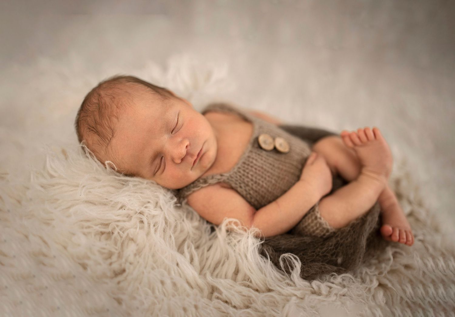 Peaceful newborn wearing gray outfit sleeping on soft white fur background.