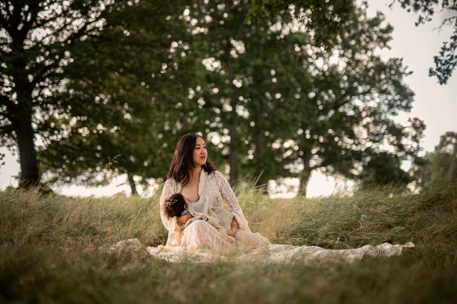 Amningsfotografering i Skåne med mamma som ammar sitt barn i blomsteräng i solnedgång.