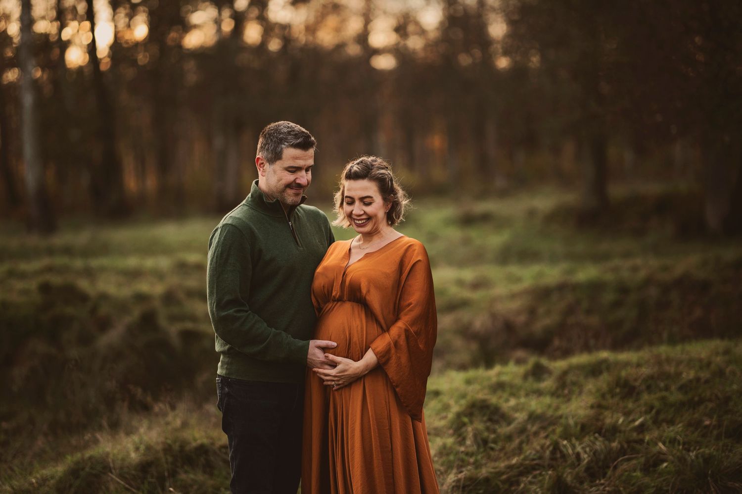 A couple poses together in autumn, wearing warm colors against natural backdrop.