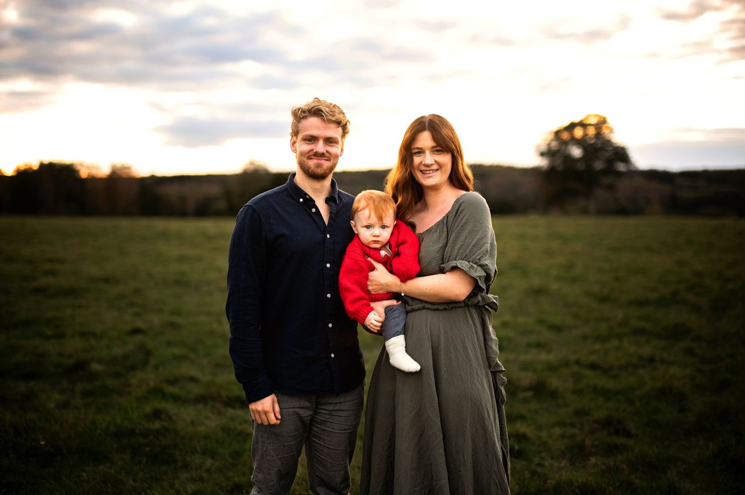 A family portrait taken at sunset in a green field with warm golden lighting.