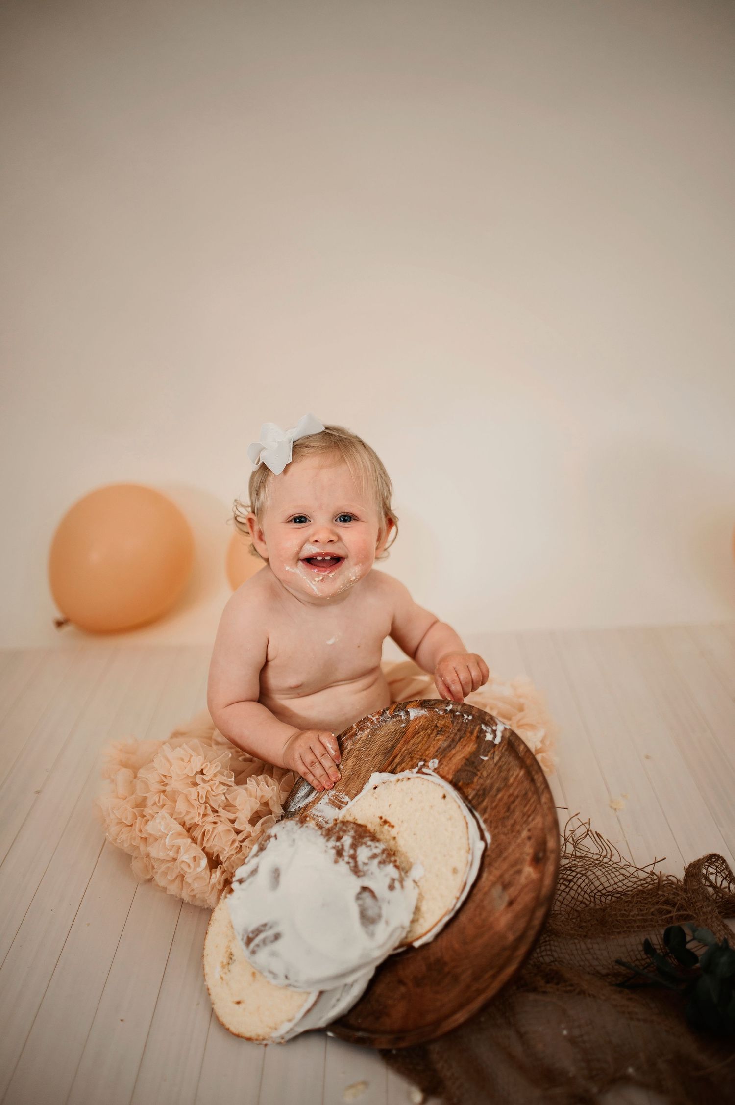 Baby in tulle skirt laughs while playing with cake during birthday photography session.