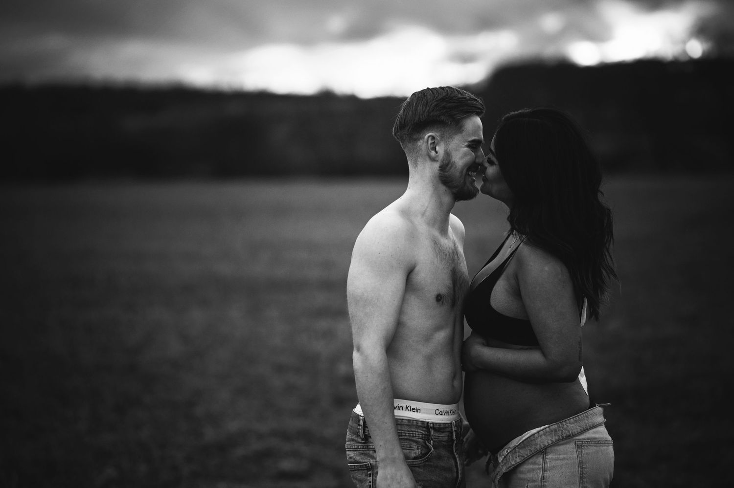 A black and white maternity photo captures an intimate moment between a couple.