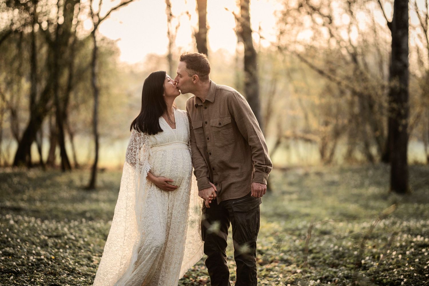 Gravid kvinna i ljus klänning och hennes partner under en gravidfotografering i skogen i Skåne.
