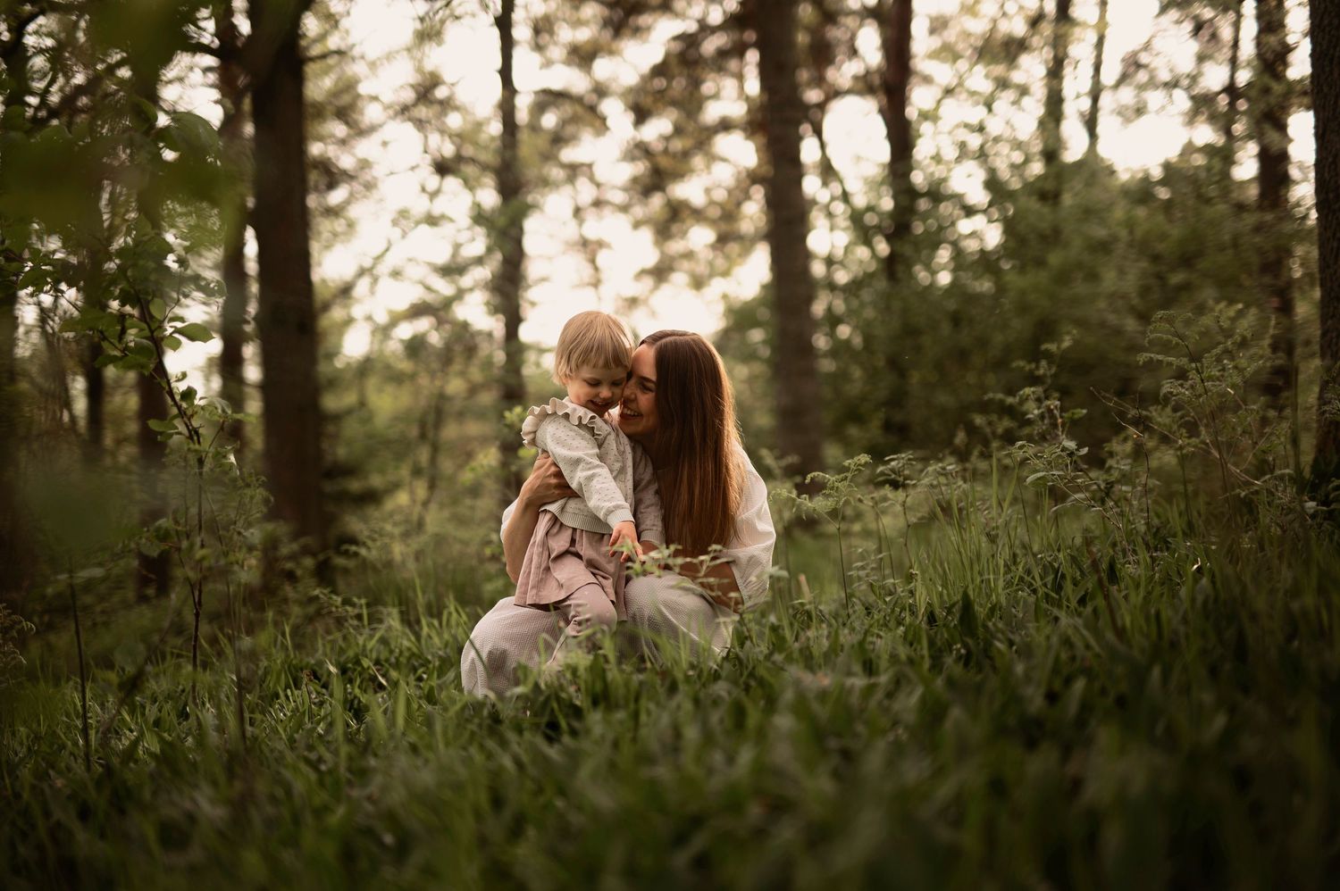 Familjefotografering i Skåne med mamma och småbarn i grön skogsmiljö i intimt ögonblick.