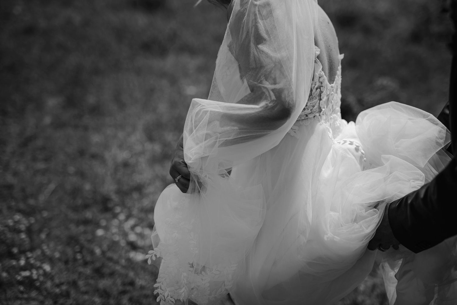 Black and white photo of a bride in a flowing wedding gown and veil, captured mid-movement outdoors.