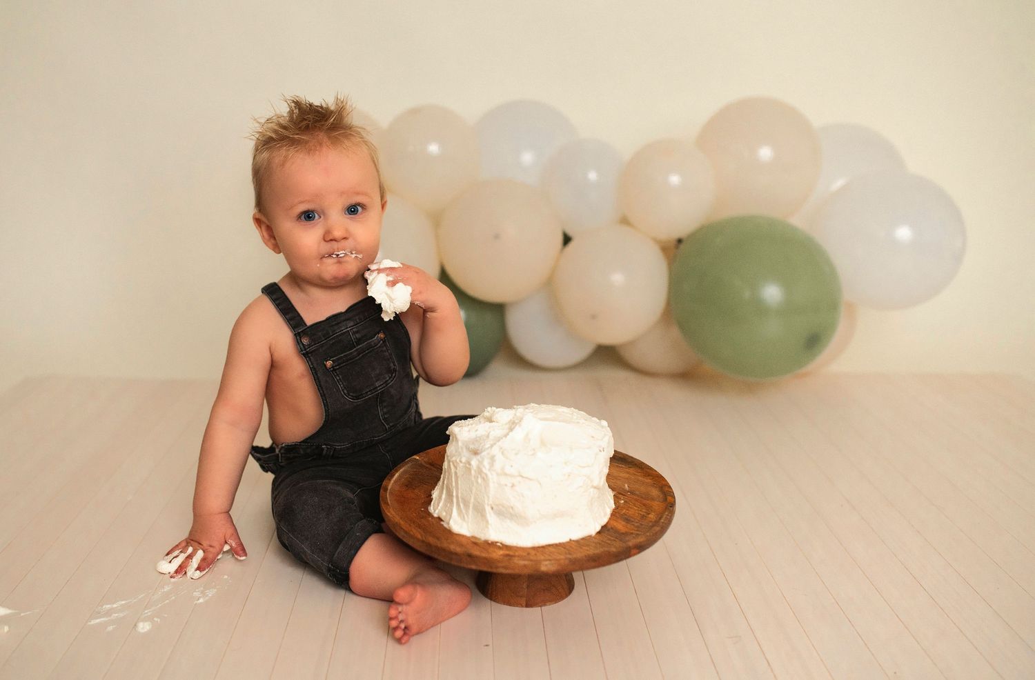 A birthday photoshoot setup with a white cake on a wooden stand and balloon decorations.