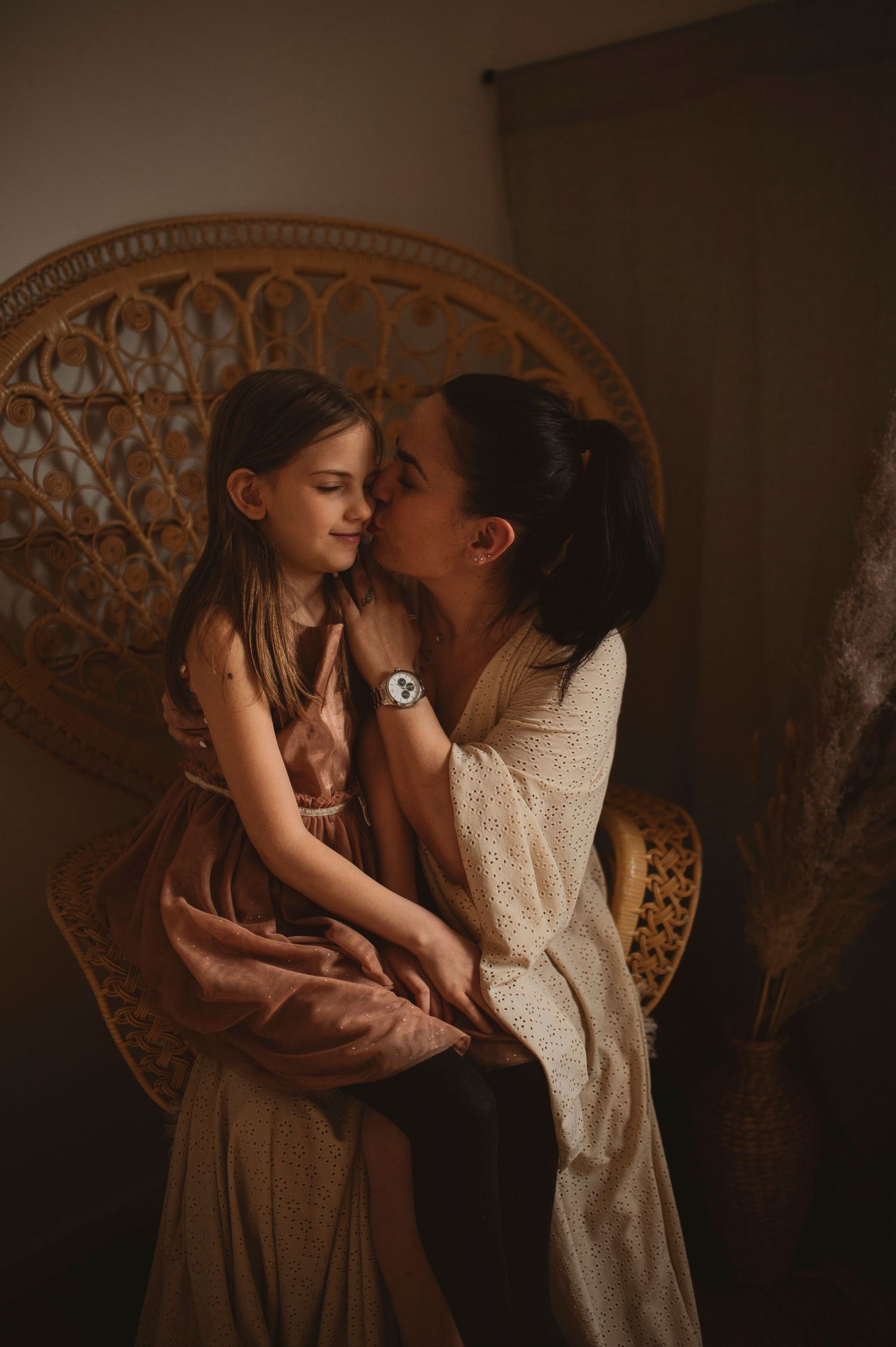 Gentle embrace photographed in moody lighting with vintage peacock chair backdrop.
