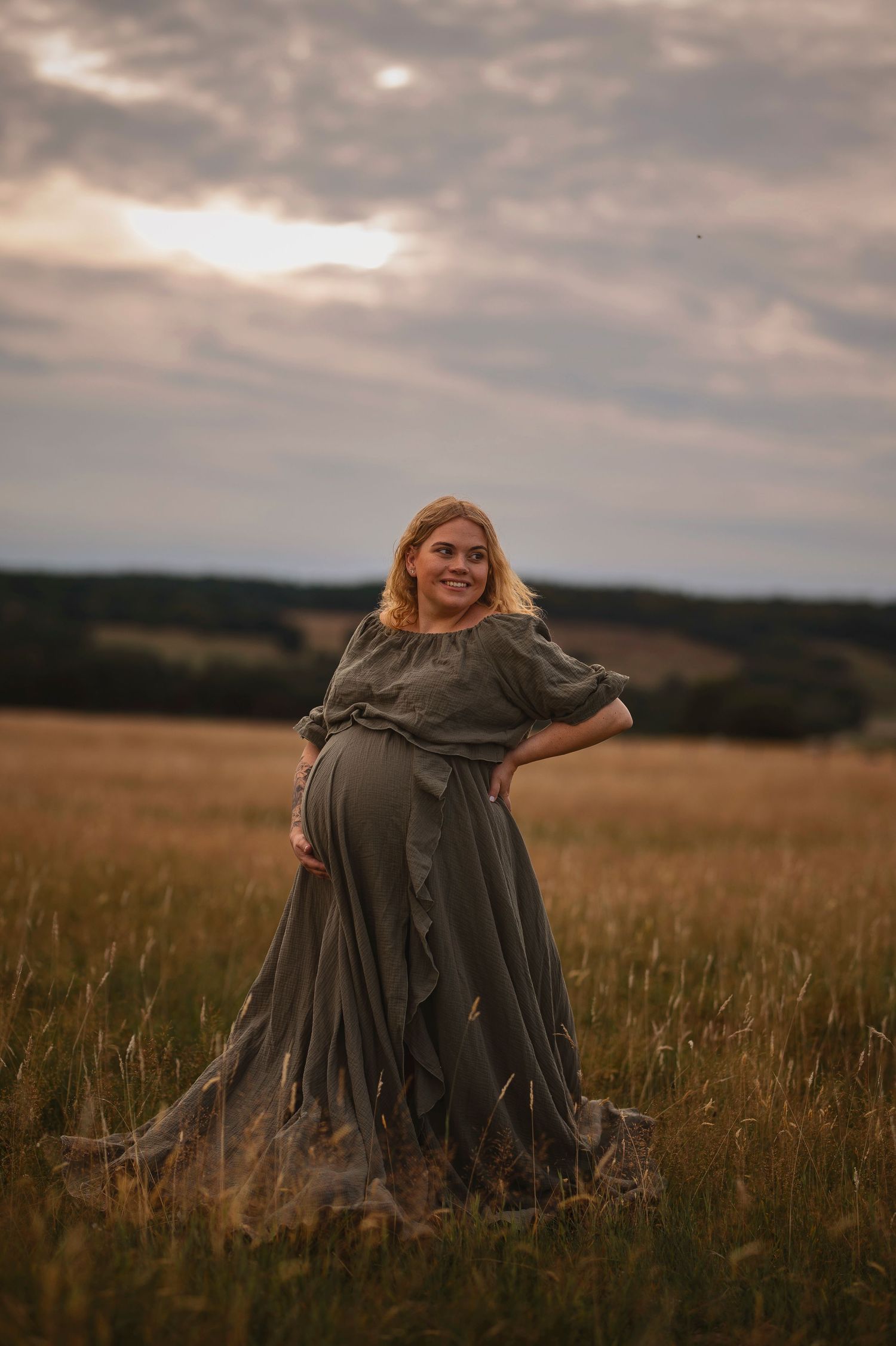 Gravidfotografering i Skåne med tvillinggraviditet som siluett mot dramatisk molnig himmel i öppet fält.
