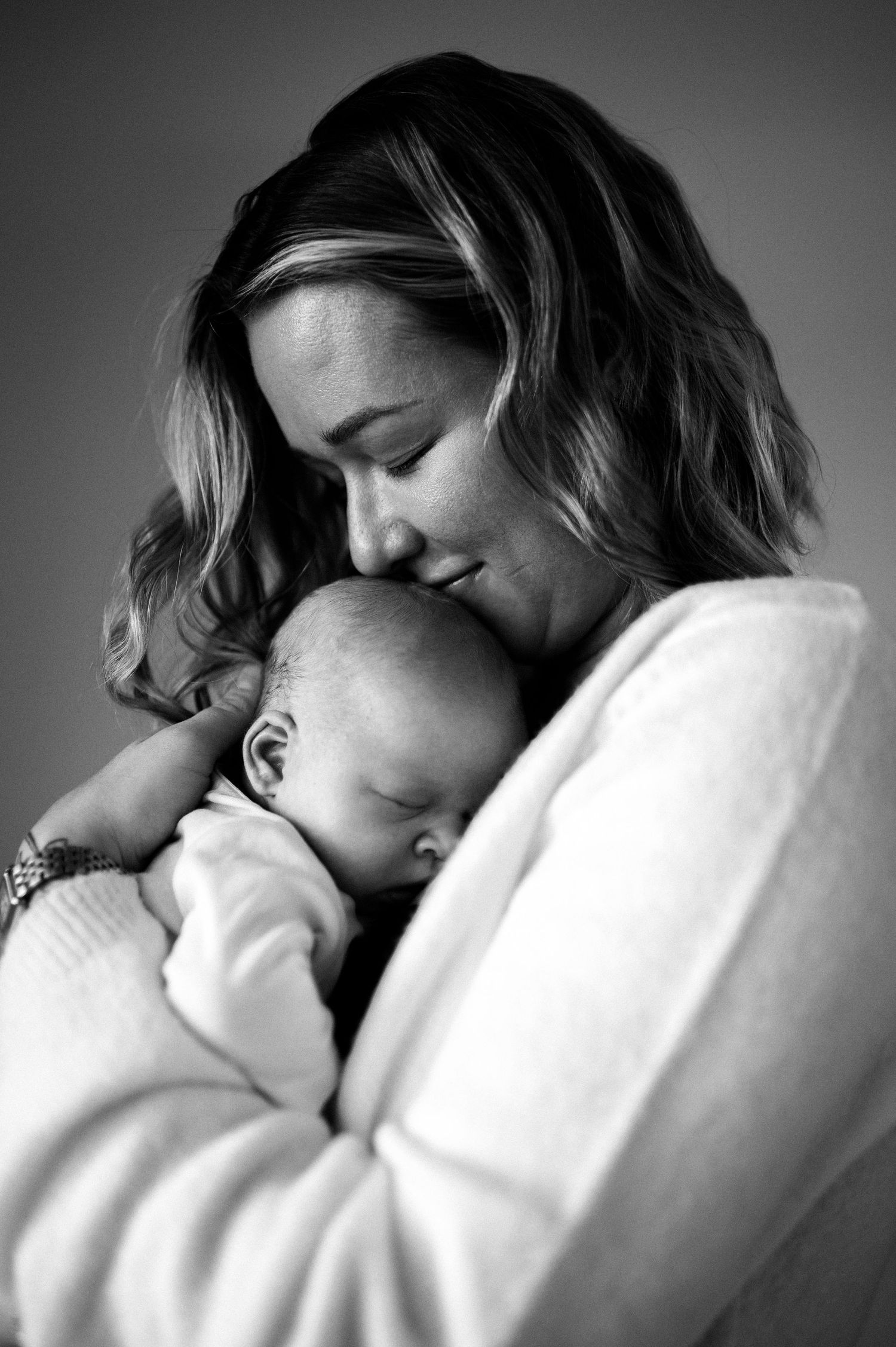 Svartvit nyföddfotografering i Hässleholm med mamma som pussar sin sovande bebis.
