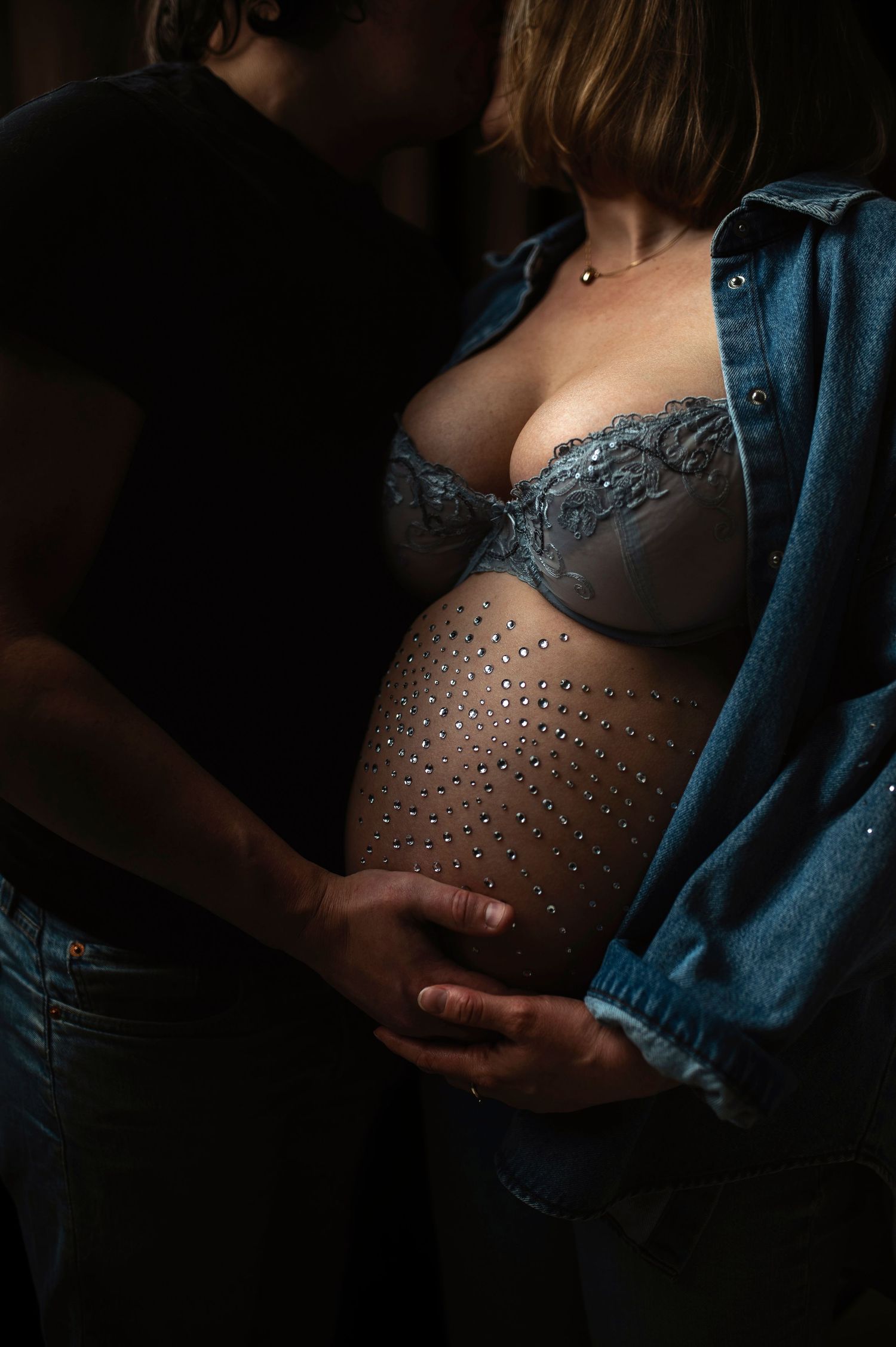 Gravidfotografering i Hässleholm med partner som håller sin hand på gravidmagen i jeansjacka i studio.