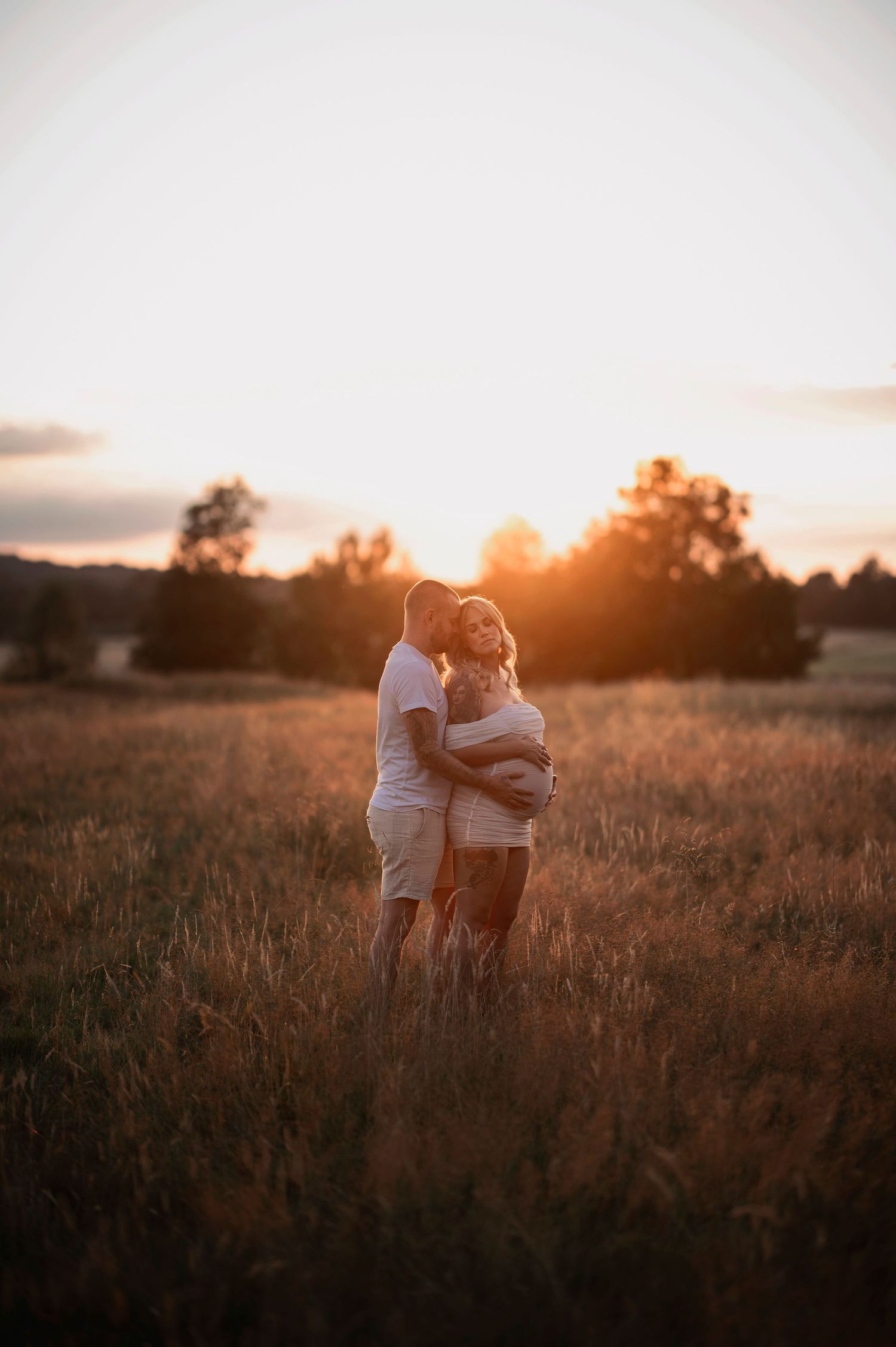 Gravidfotografering i Skåne med blivande föräldrar i solbelyst äng i gyllene kvällsljus.