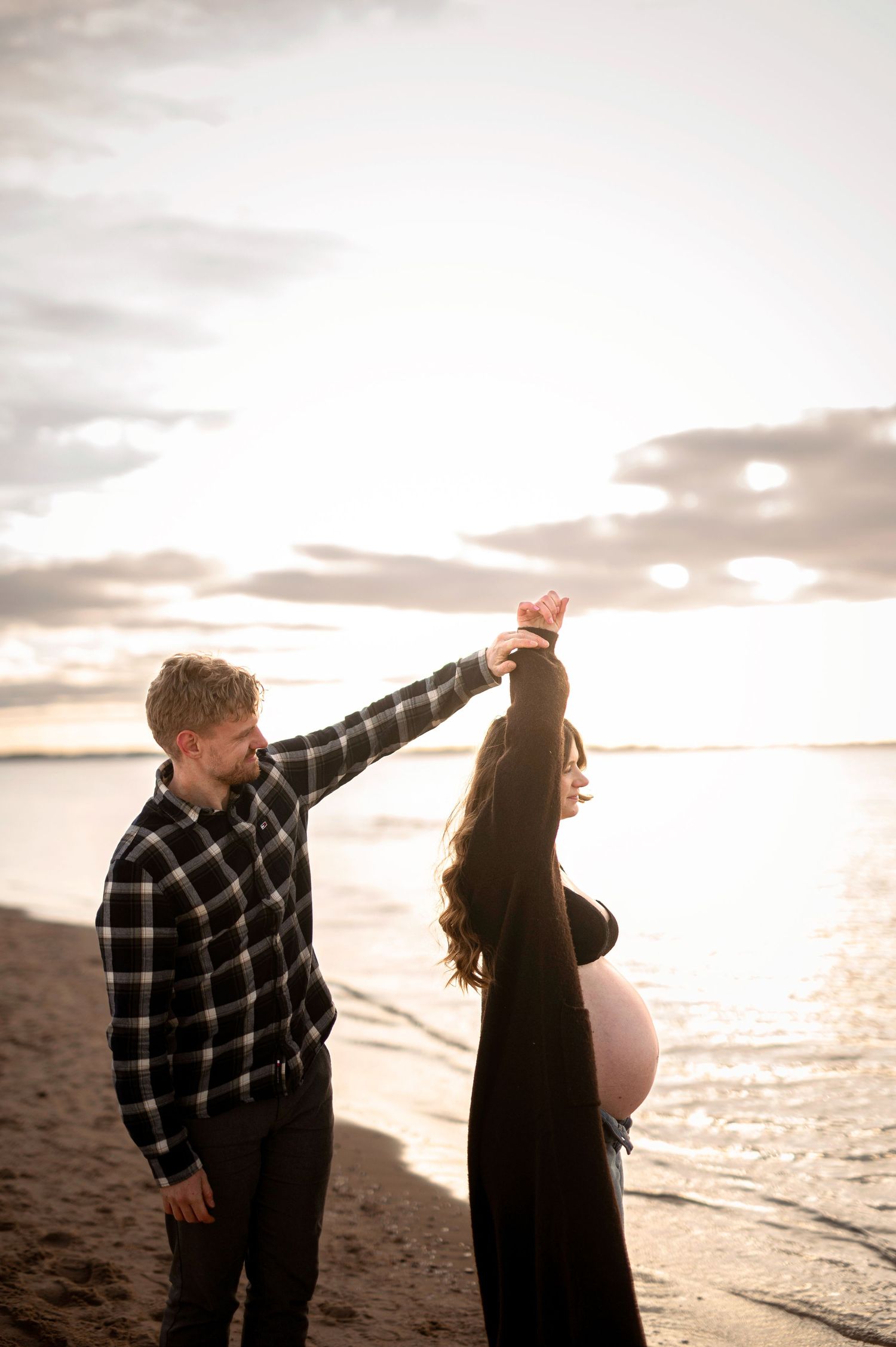 Gravidfotografering i Skåne med blivande föräldrar som dansar vid havet i solnedgången.