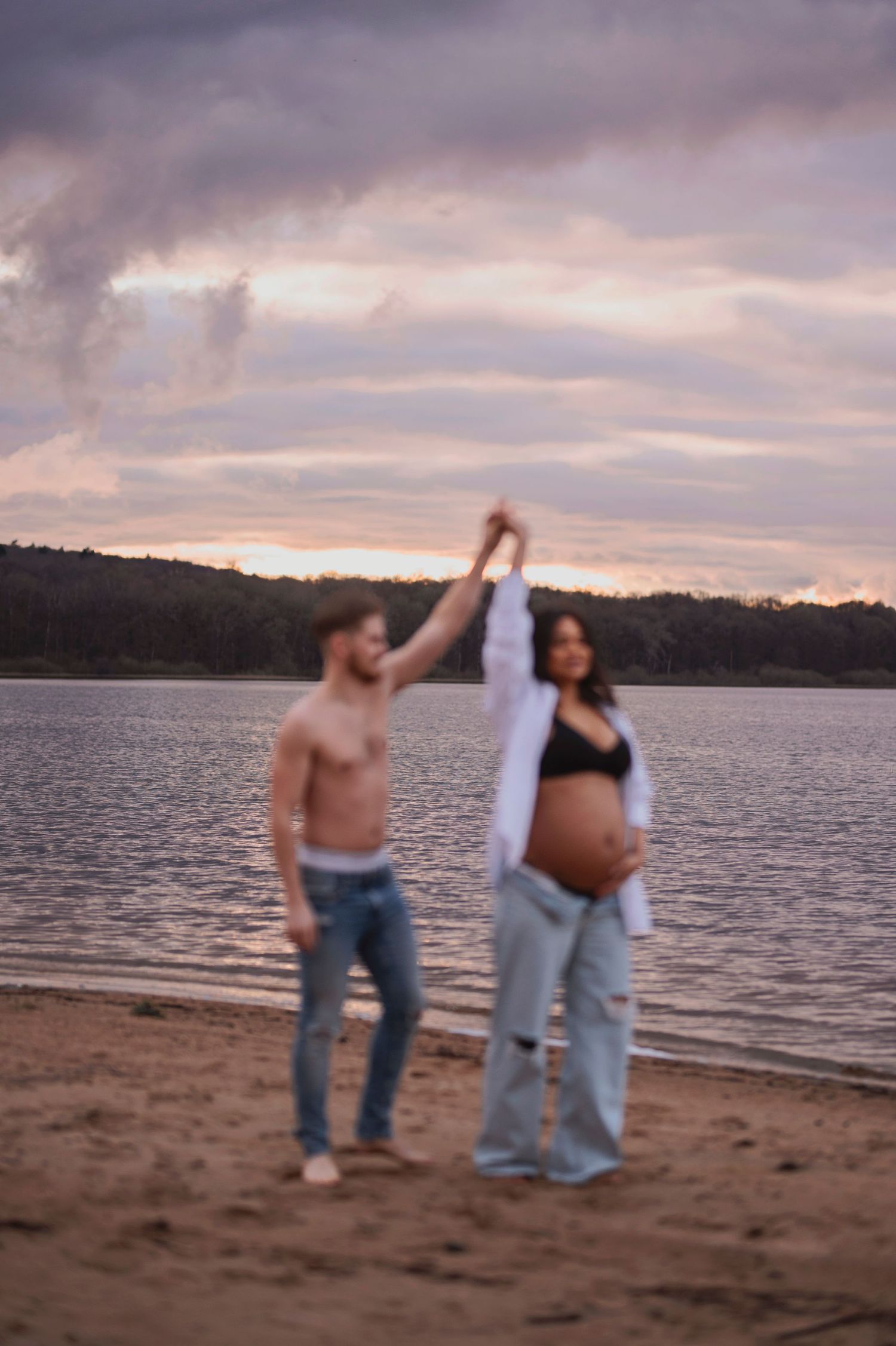 A couple dances on a beach at sunset with their hands raised against a purple sky.