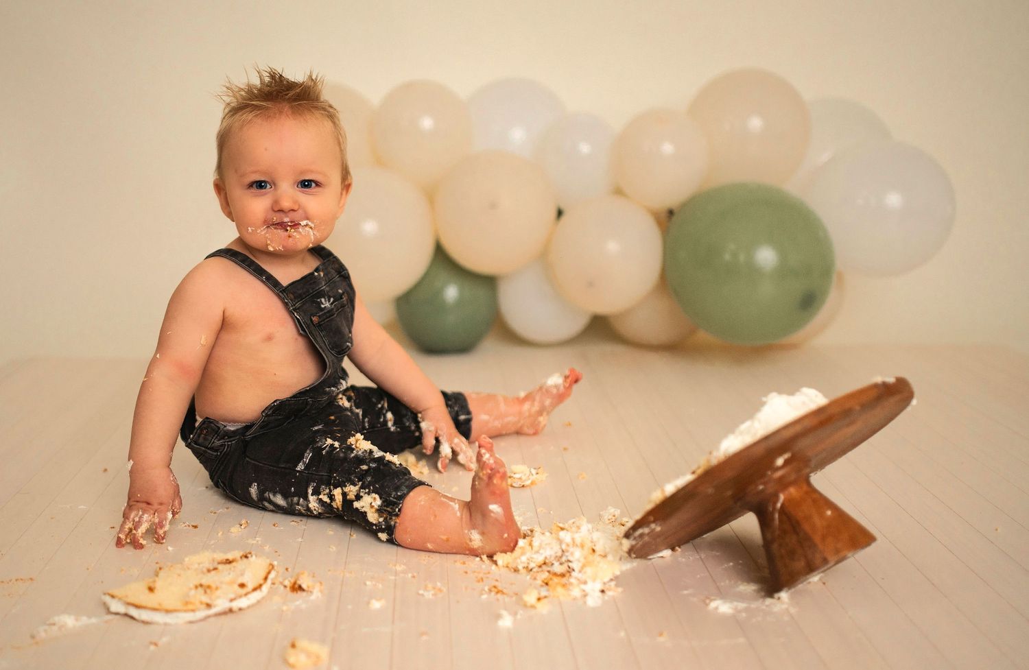 A messy cake smash photoshoot setup with white and sage green balloons in the background.