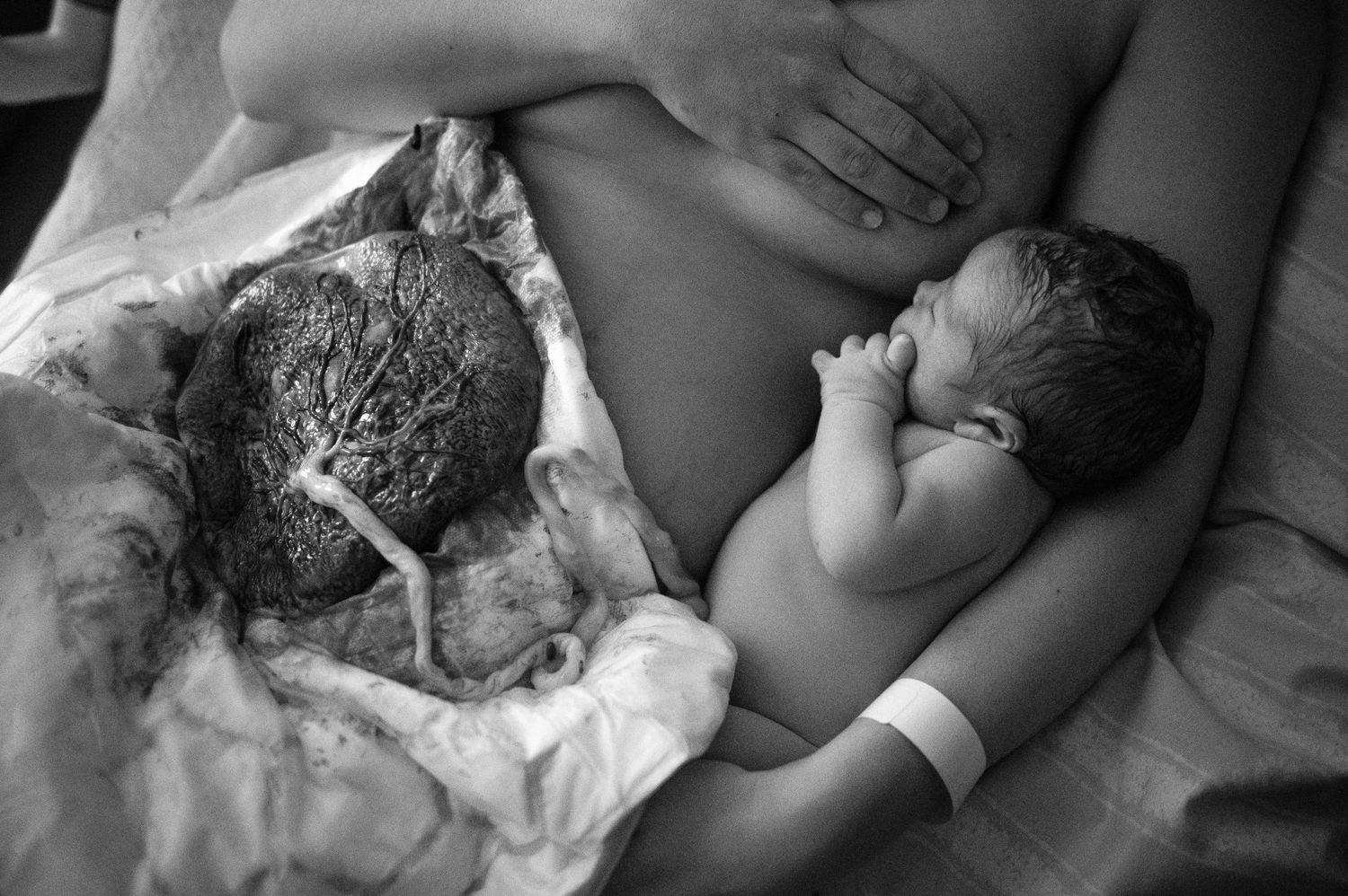 A black and white image shows a newborn baby resting peacefully on a textured blanket.