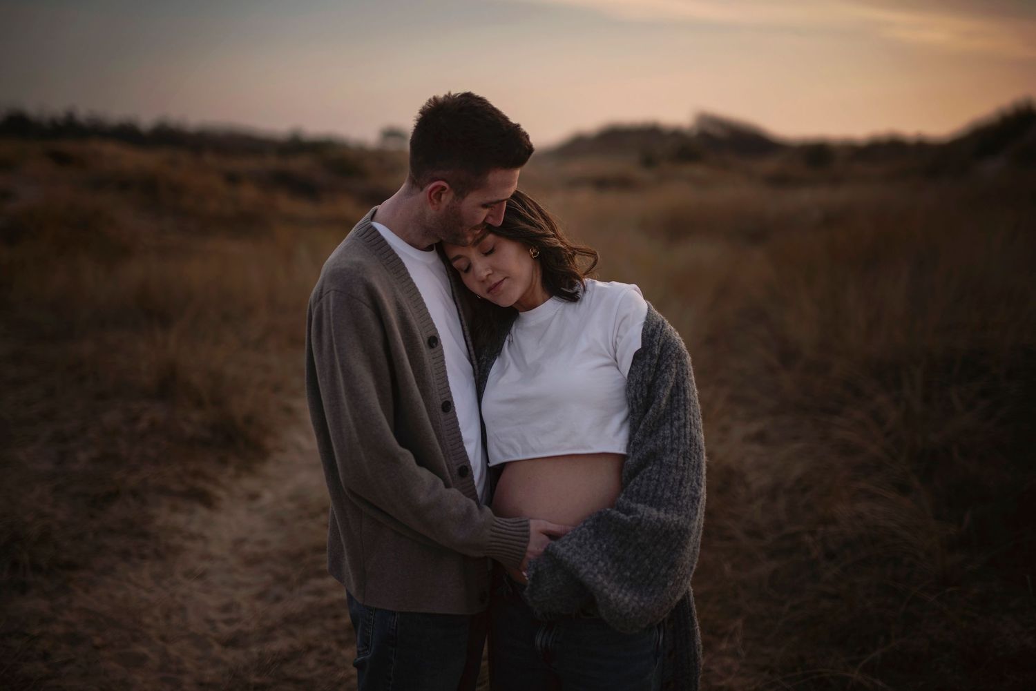 An intimate couple embraces in a serene desert landscape at dusk, creating a romantic silhouette against the warm sky.