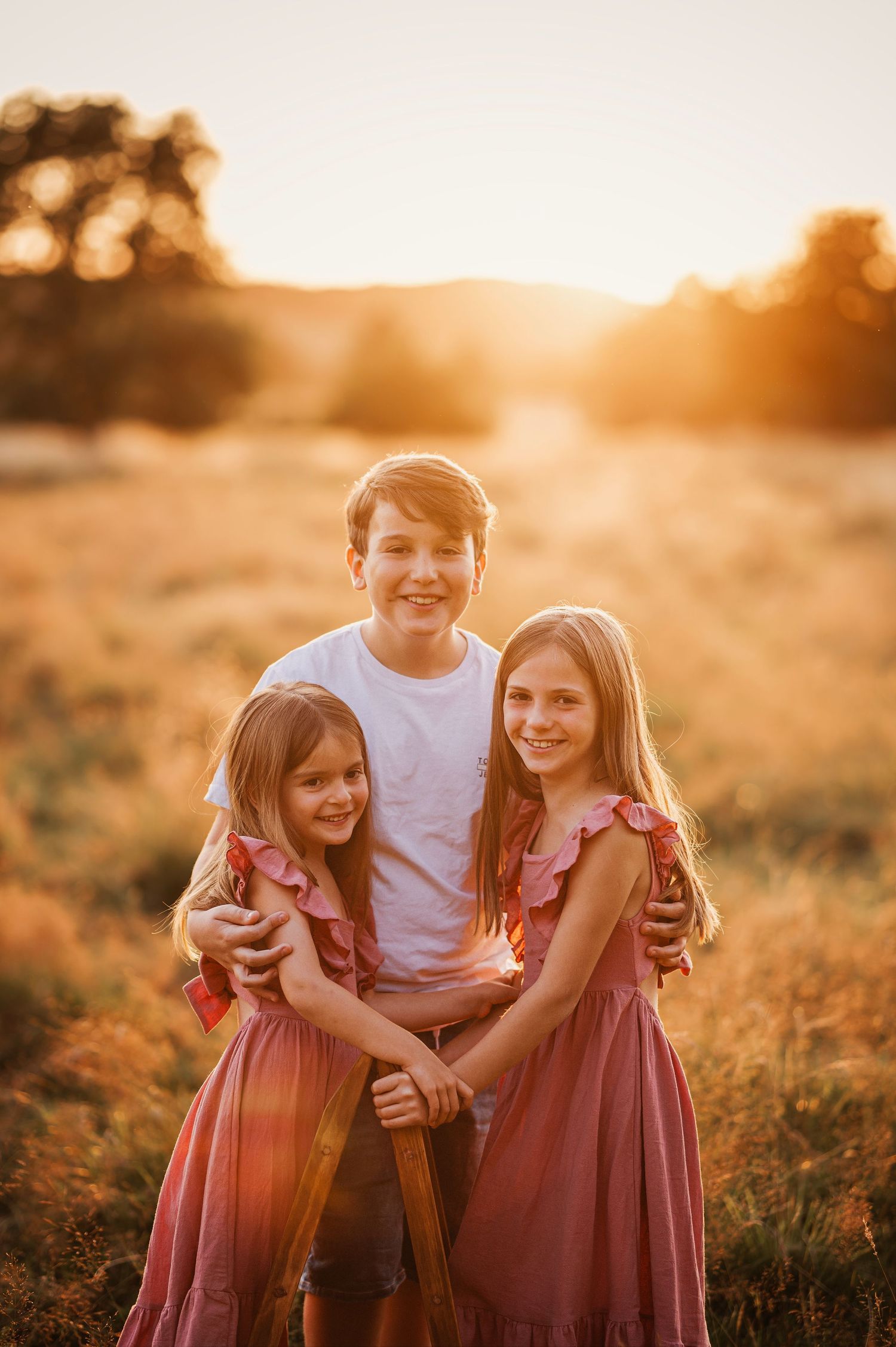 Three siblings pose together in matching outfits during sunset photoshoot.