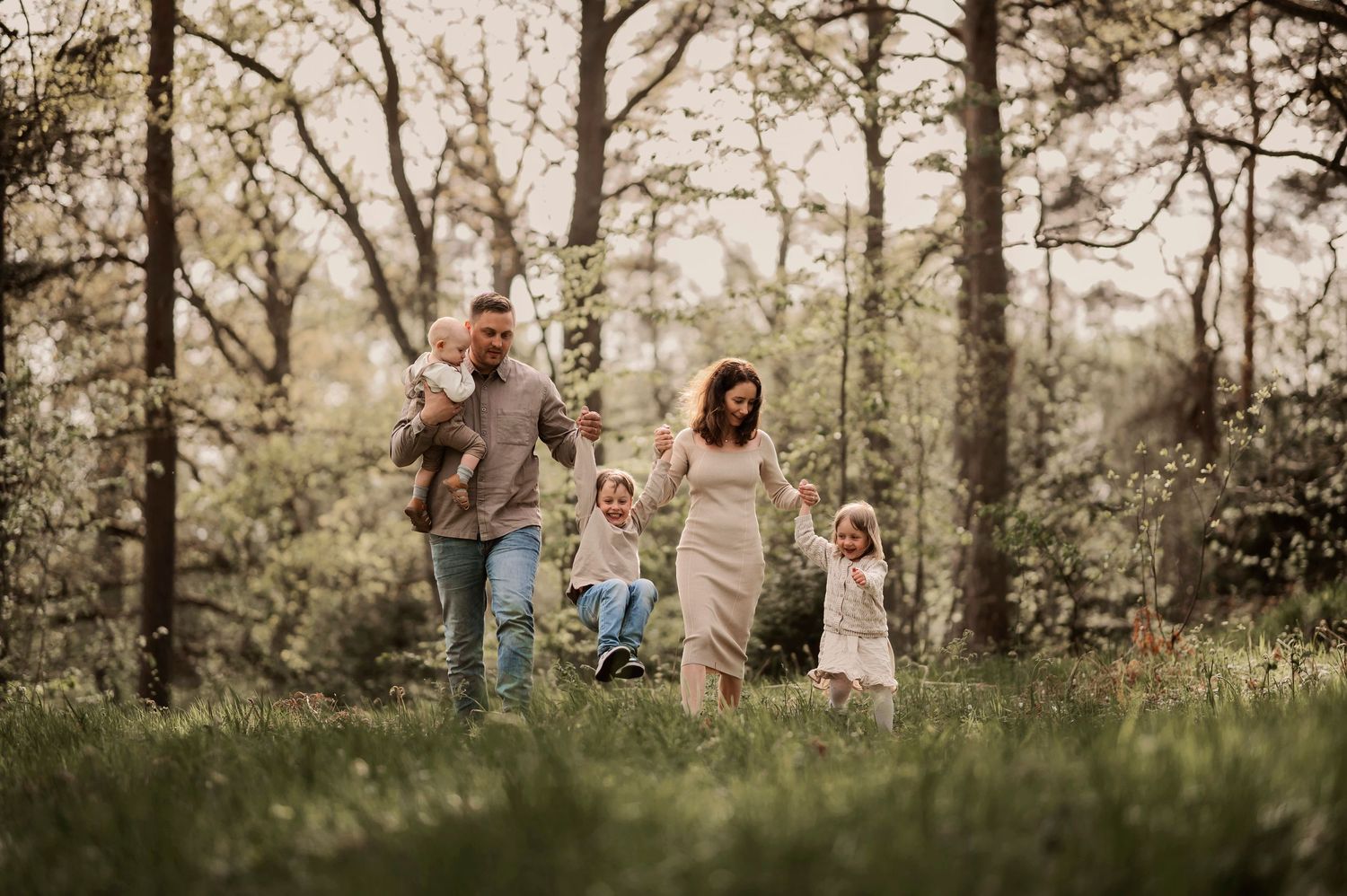 Familjefotografering i naturen där en familj på fem går hand i hand genom en grönskande skog under våren.